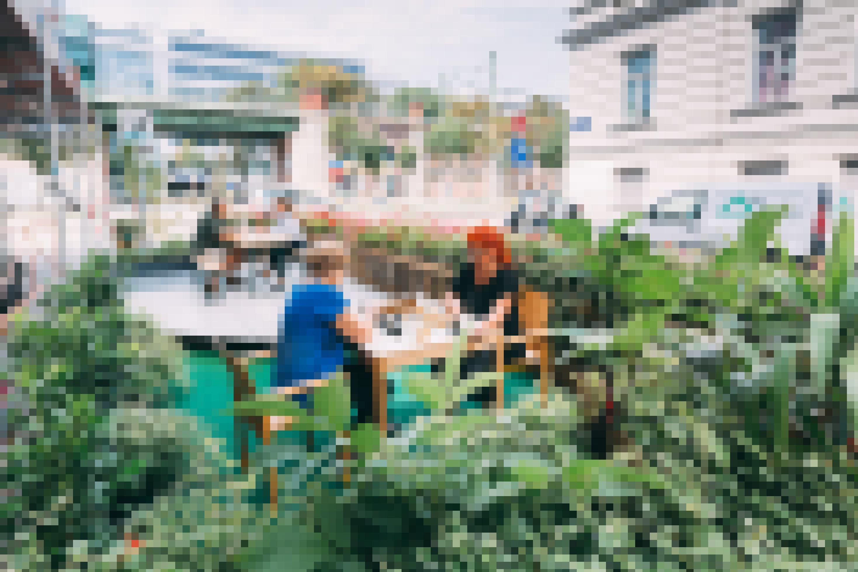 Auf den Parkplatz wurde eine Terrasse gebaut, die mit Blumen und Grünpflanzen eingefasst ist. An einem Tisch spielen zwei Frauen Schach, an einem anderen Tisch unterhält sich ein Paar.