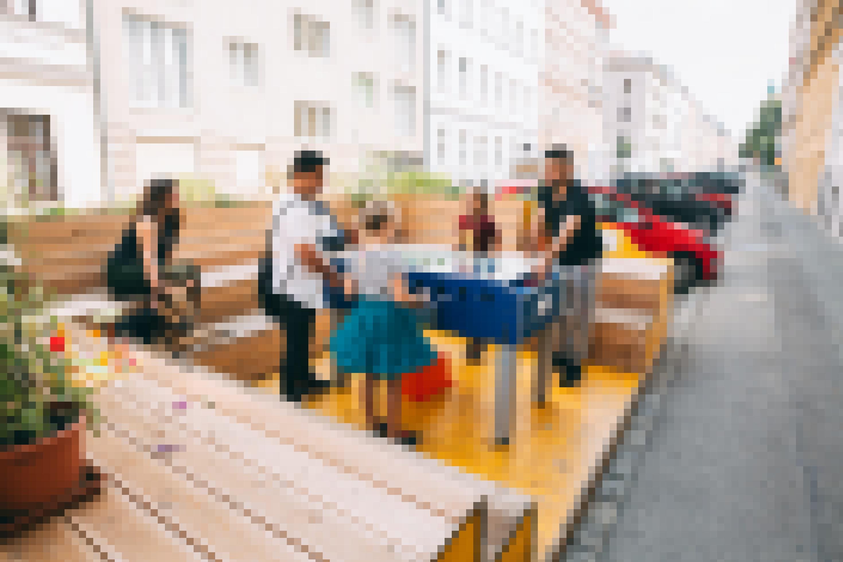 Auf dem Parkplatz steht eine Holzterrasse mit Blumenkästen und Holzbänken. In der Mitte steht ein Kicker an dem zwei Männer mit zwei Mädchen gegeneinander spielen. Eine Frau mit Schäferhund sitzt auf der Bank und schaut ihnen zu