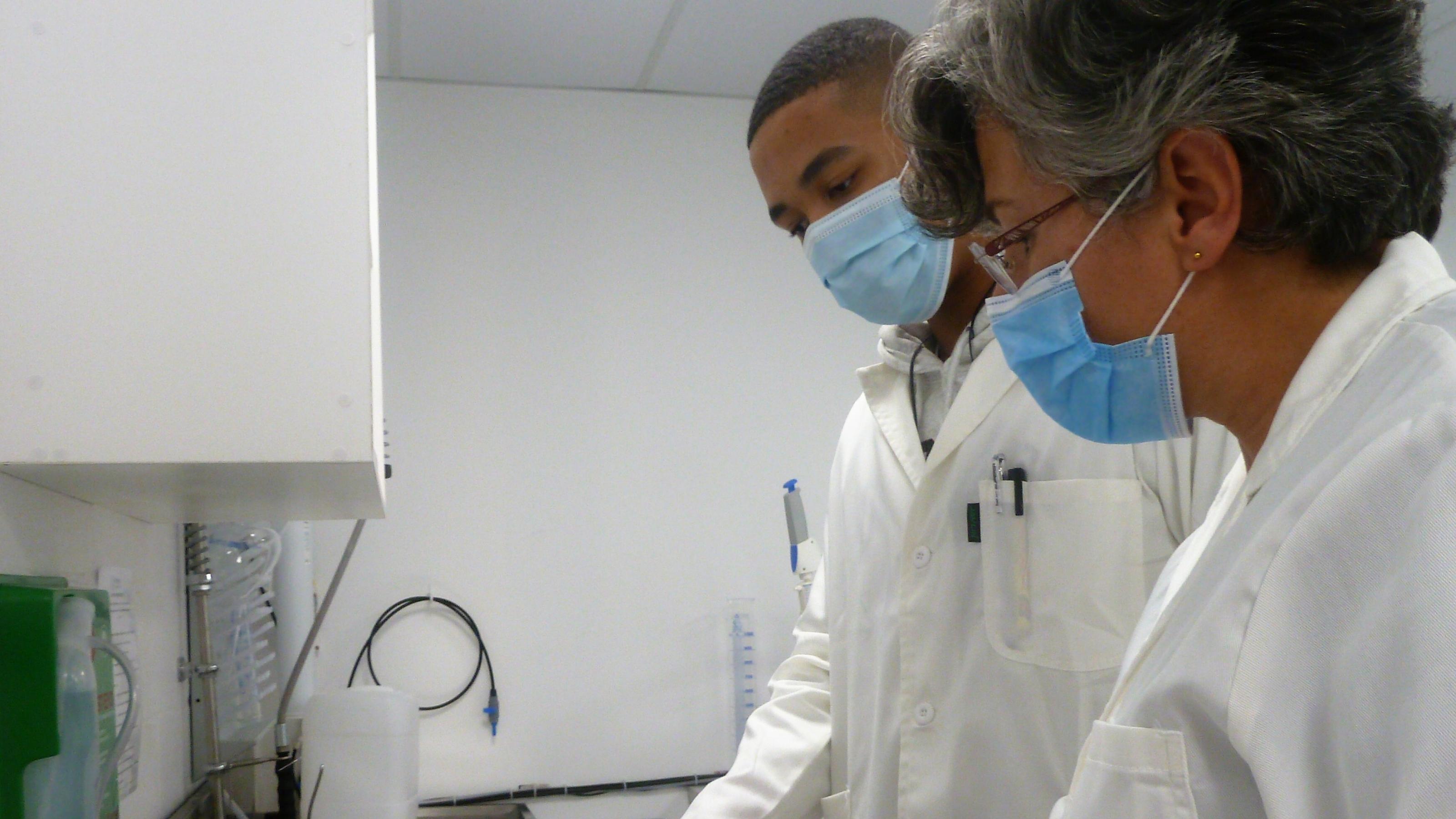 Zwei Forschende mit Masken, eine Frau und ein Mann, schauen im Labor auf die Anzeige eines Labor-Geräts