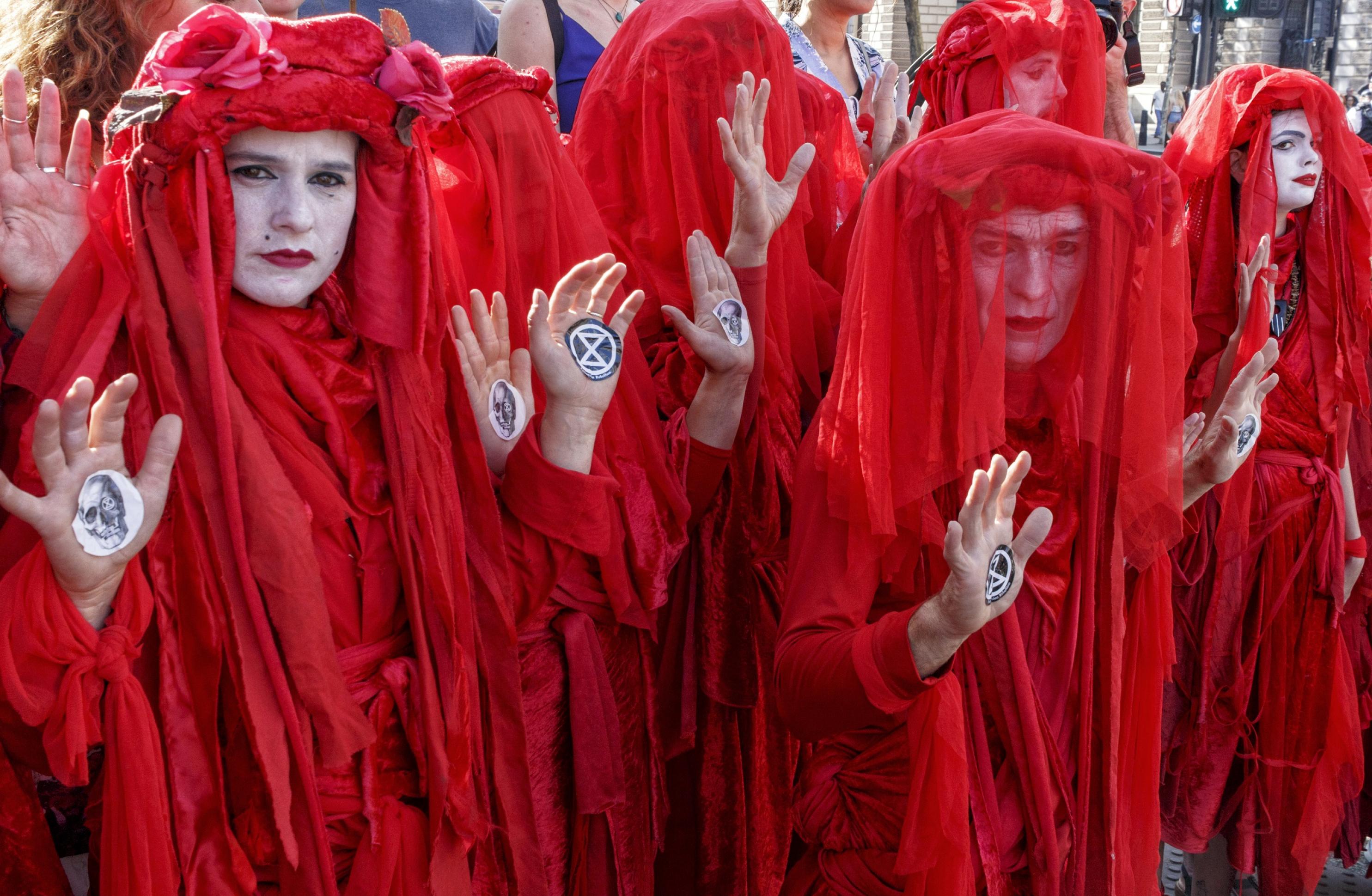 Die Aktivistengruppe RedRebell-Brigade bei einer Demonstration von Extinction Rebellion. Die Aktivisten sind komplett in rote Gewänder gehüllt und sie tragen weiße Masken.