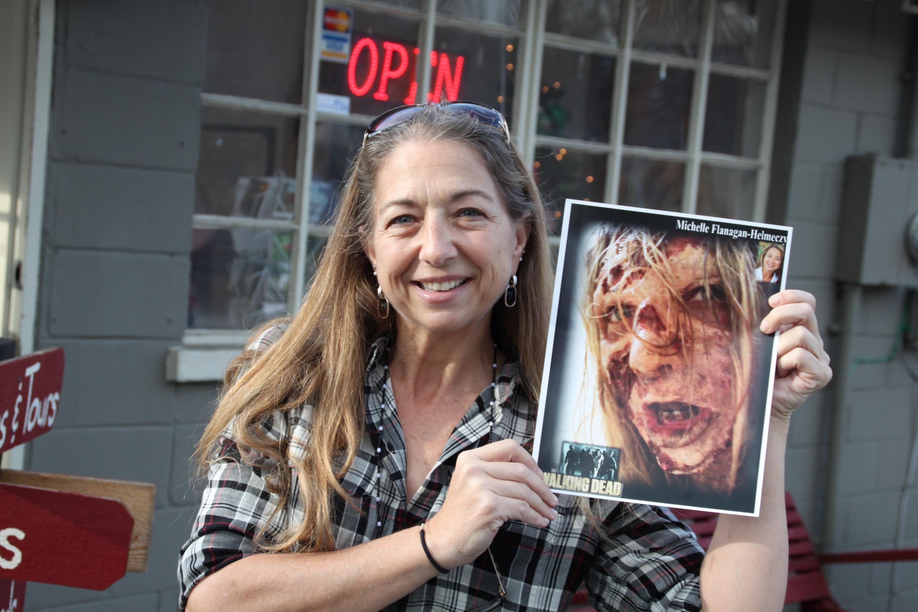 Eine lächelnde Frau hält ein gerahmtes Porträt von einem Zombie.