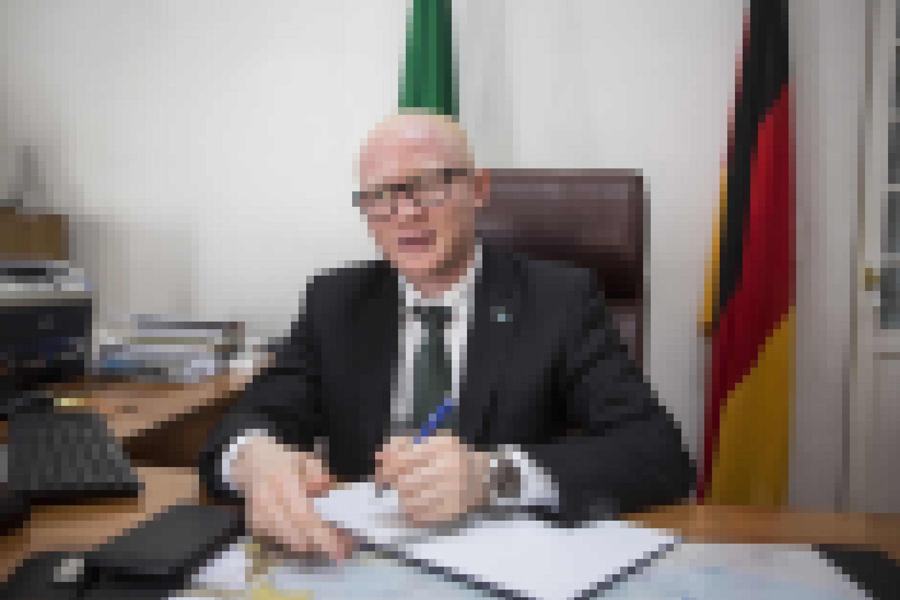 Das Bild zeigt den Botschafter von Tansania in Deutschland, Dr. Abdallah Possi, an seinem Schreibtisch in der Botschaft in Berlin. Im Hintergrund die Flaggen von Tansania und Deutschland.