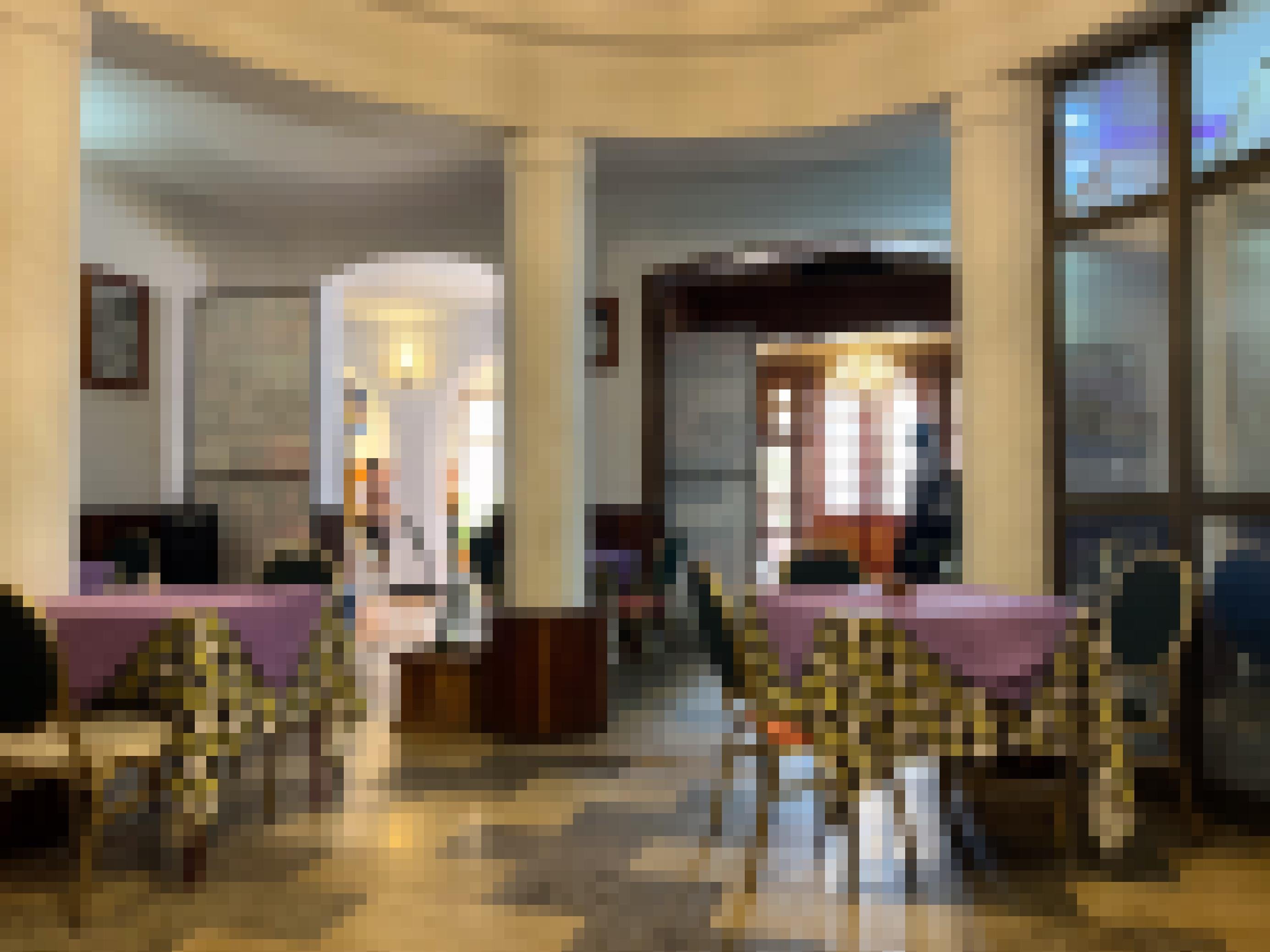 Ein Cafe im Art Deco - Stil: Man sieht einen Bereich, der mit Säulen abgegrenzt ist, oben leicht gebogene Durchgänge. gene