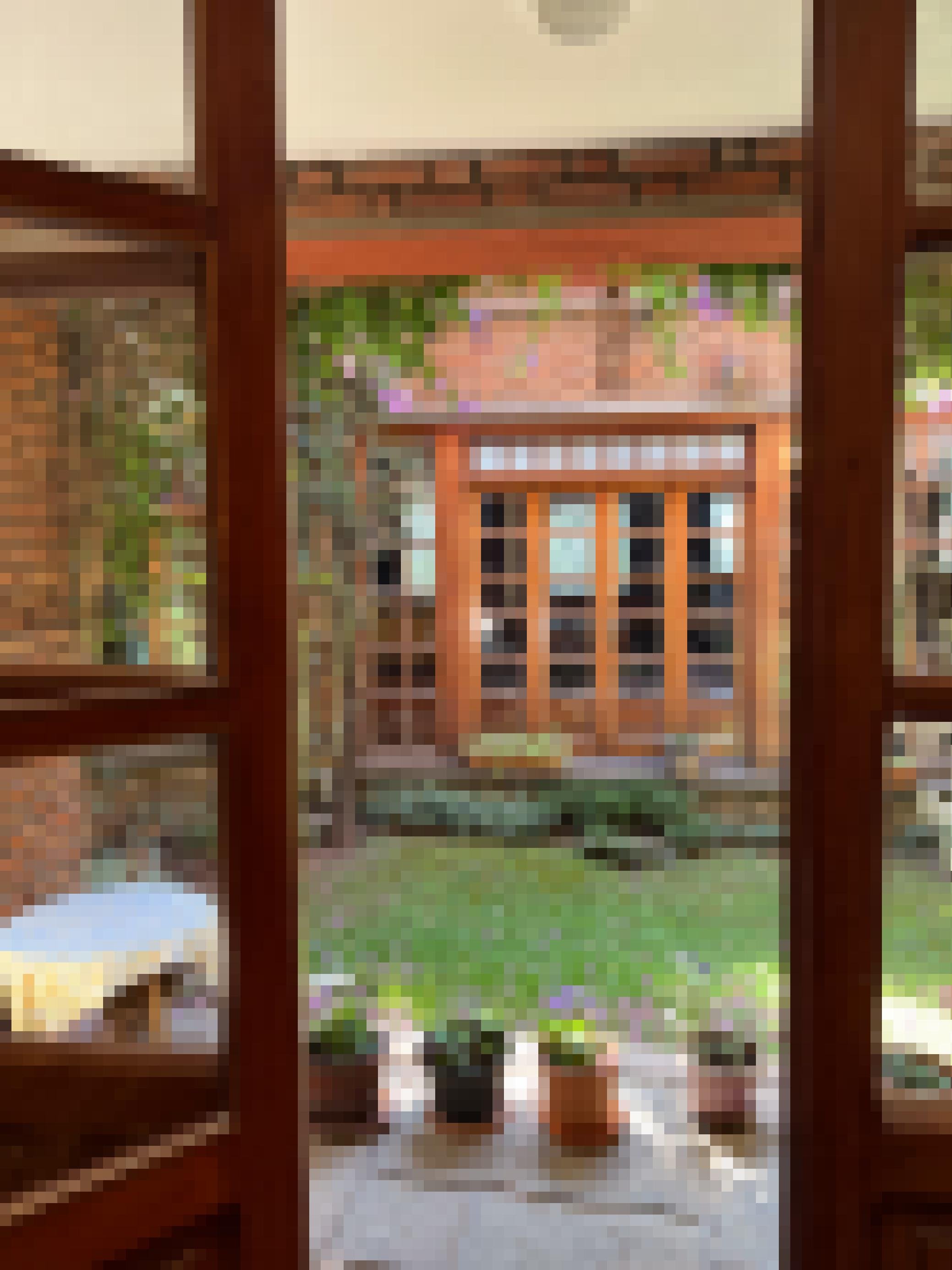 Durch eine offene Glastür fällt der Blick in einen Innenhof. Er ist mit Gras bewachsen und hat eine eigene kleine Terrasse. Auf der Rückseite des Innenhofes ist eine weitere, zweiflügelige Glastür zu sehen, der Innenhof ist also auch von dem gegenüberliegenden Zimmer aus zu betreben.
