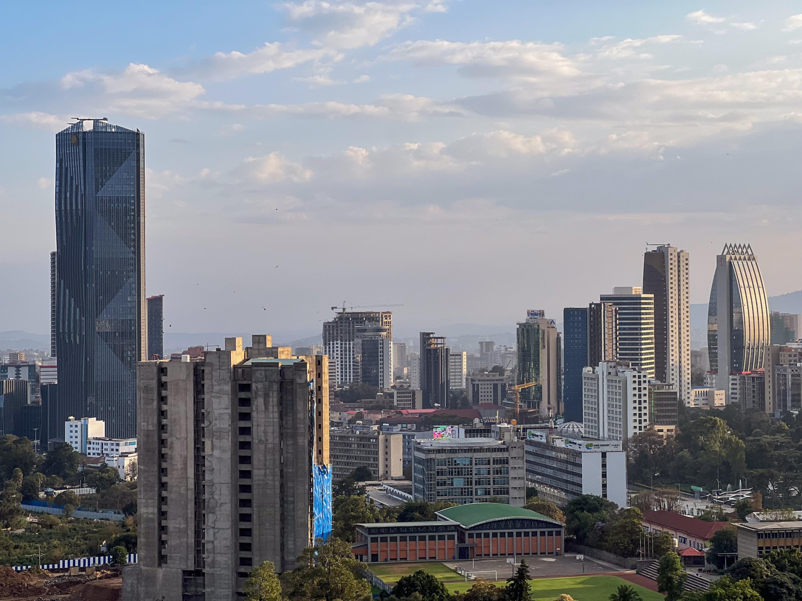 Eine Skyline in der späten Nachmittagssonne. Im Vordergrund ein Hochhaus im Bau, dahinter mehrere fertige Türme. Einer davon mit geschwungener Fassade.