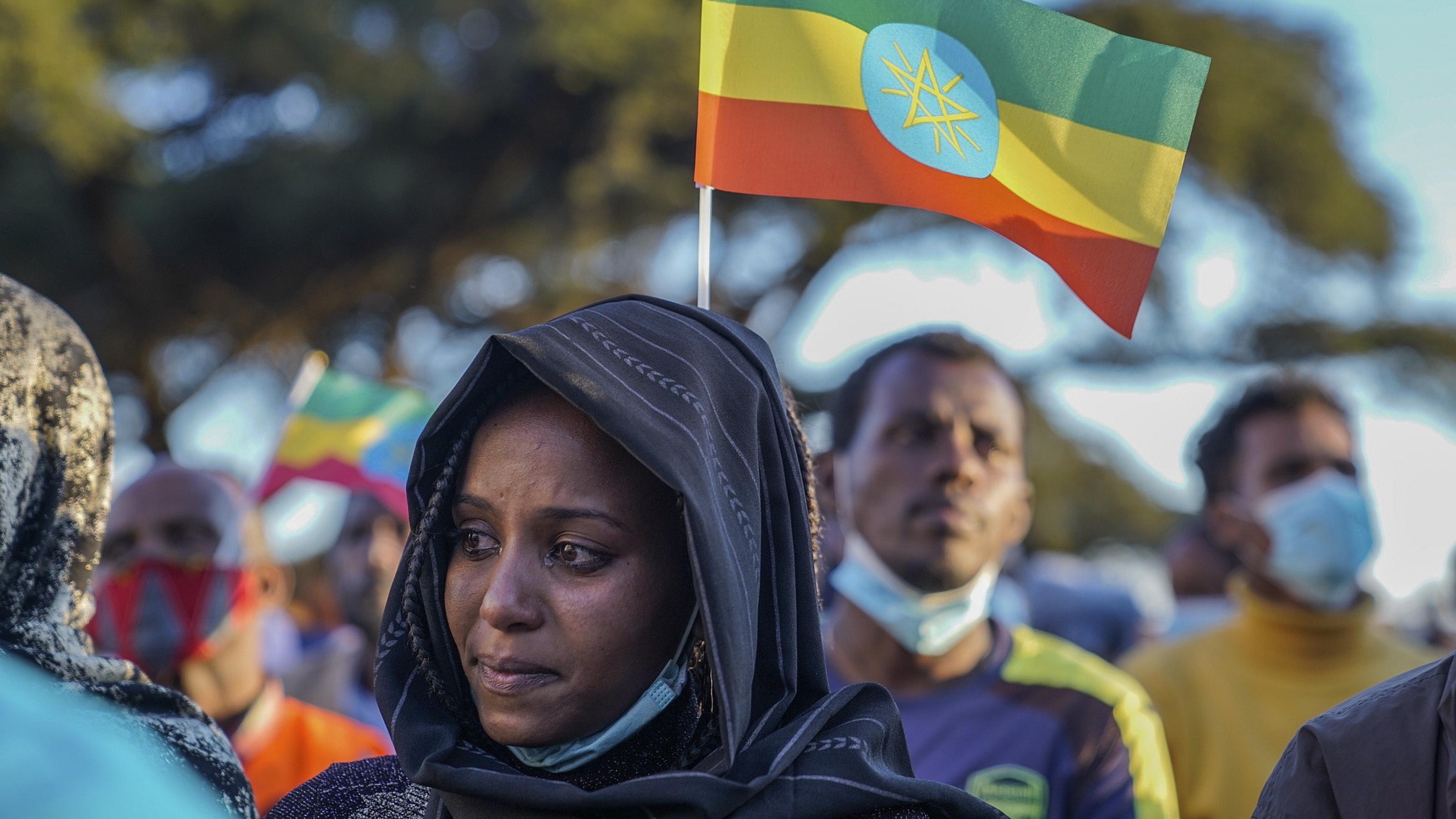 Im Vordergrund ist eine Frau in Großaufnahme zu sehen, sie weint. Im Hintergrund eine äthiopische Flagge: Grün-gelb-rot quer gestreift, in der Mitte das aktuelle Hoheitszeichen, ein strahlendes Pentagramm. Dahinter weitere Demonstrierende.