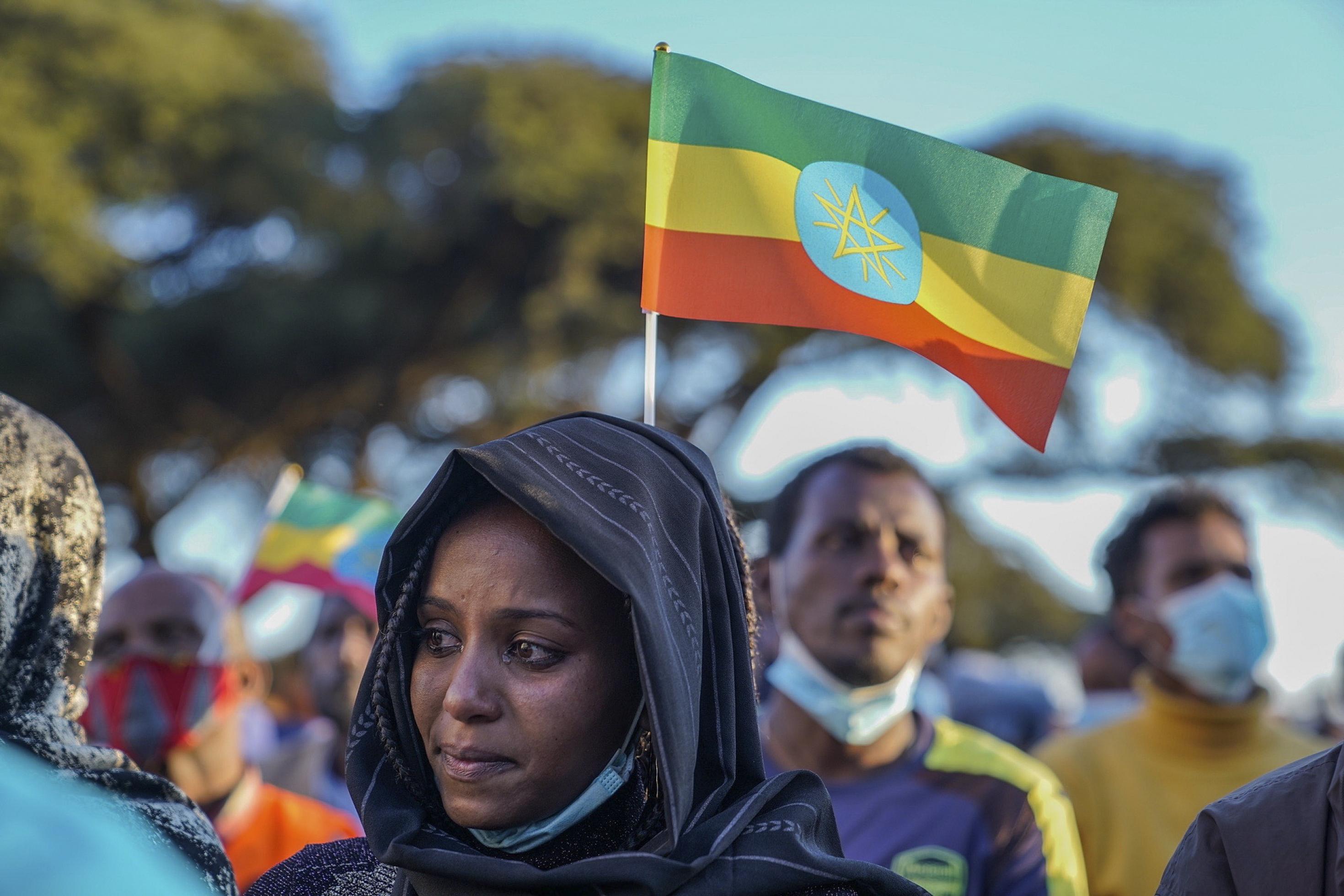 Im Vordergrund ist eine Frau in Großaufnahme zu sehen, sie weint. Im Hintergrund eine äthiopische Flagge: Grün-gelb-rot quer gestreift, in der Mitte das aktuelle Hoheitszeichen, ein strahlendes Pentagramm. Dahinter weitere Demonstrierende.