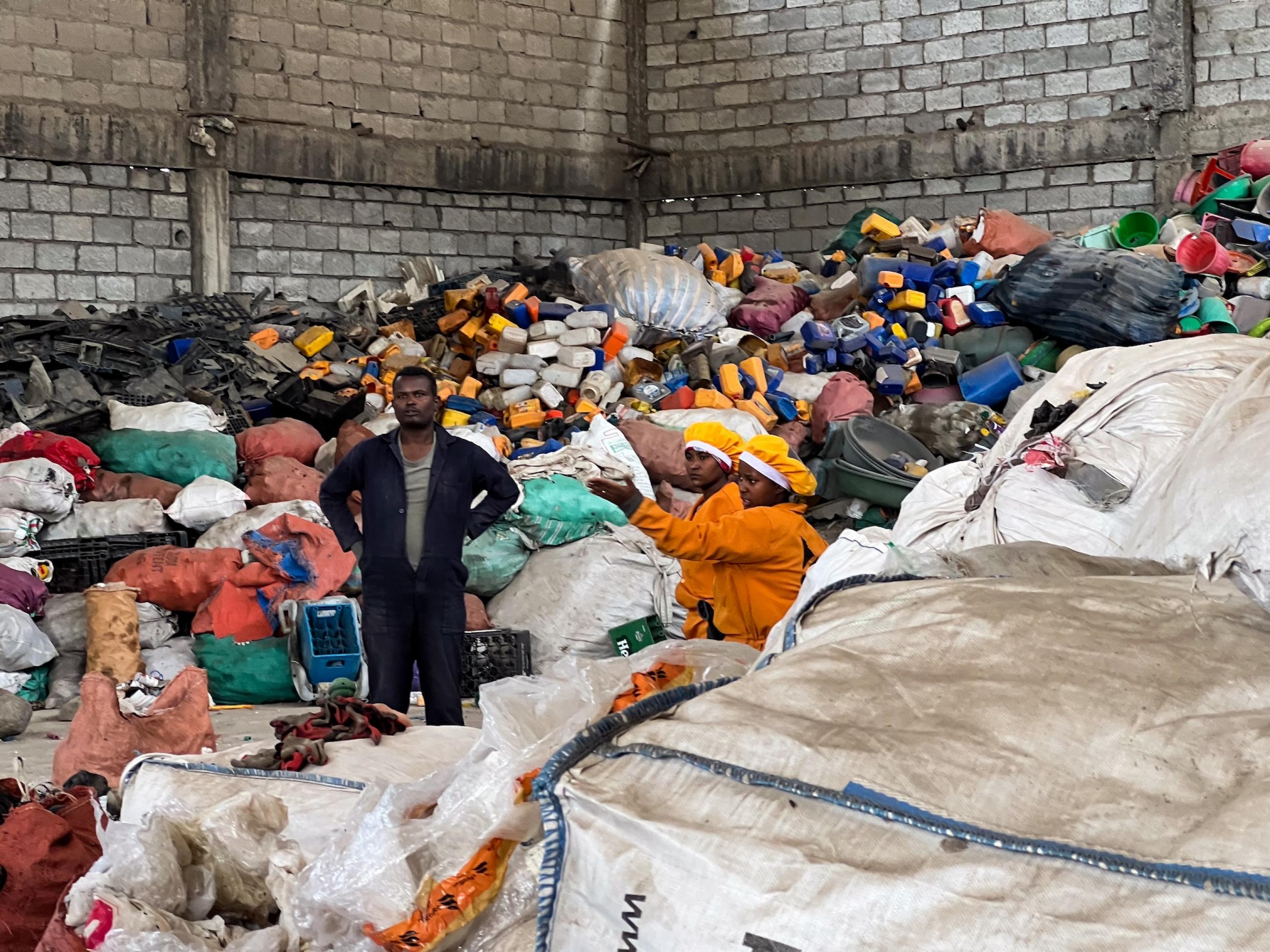 Eine Halle voller Plastikmüll und Säcken, darin sind die drei Menschen leicht zu übersehen.