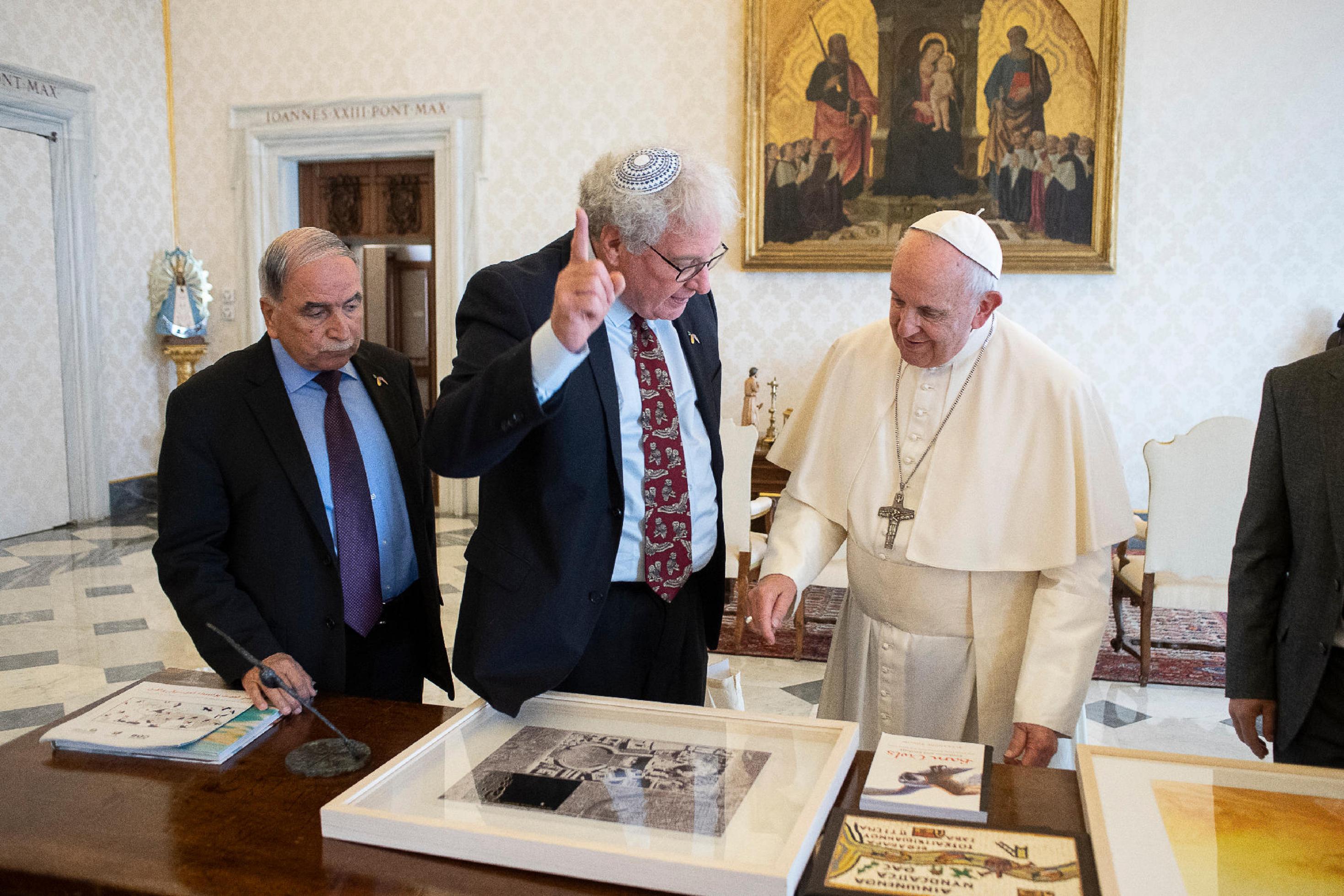 Yossi Leshem, Mansour Abu Rashid und Papst Franziskus stehen im Vatikan vor einem Tisch mit Vogelbildern.