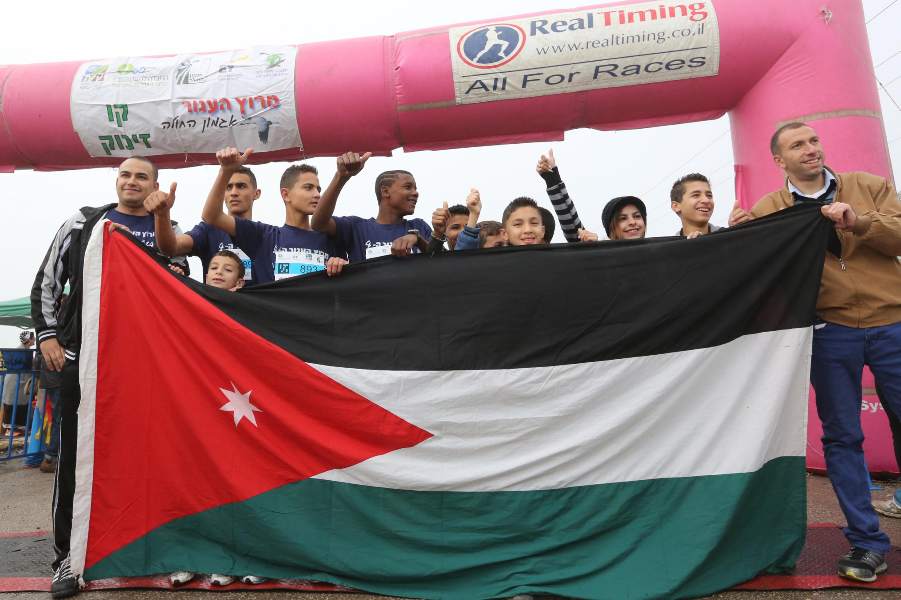 Jugendliche Jungen und Mädchen hinter einer großen Jordanien-Flagge unter dem Zieleinlauf des Kranich-Rennens im Hula-Tal.