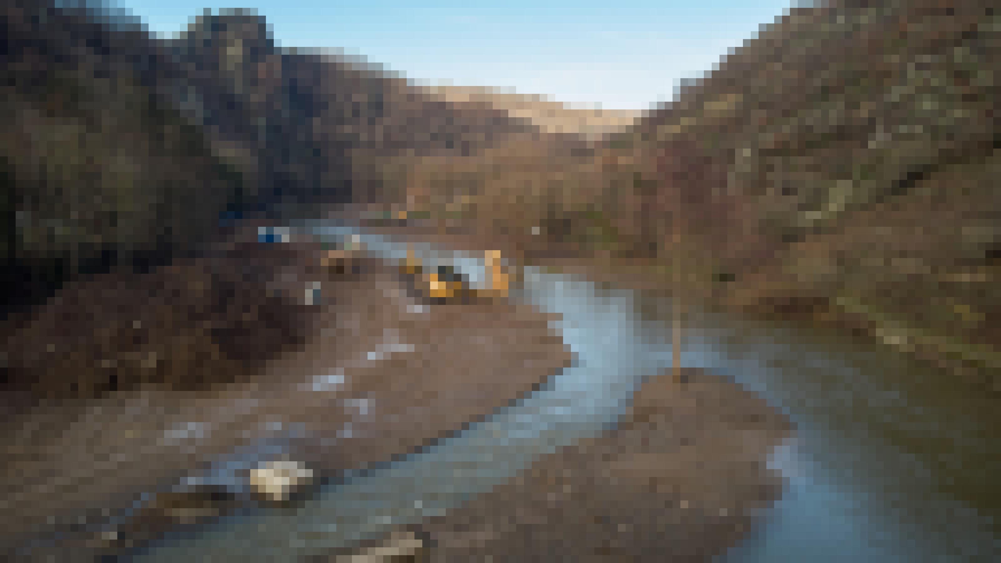 Der Fluss fliesst zwischen Steilhängen. Der Talboden ist abgetragen, Baufahrzeuge stehen am Fluss.