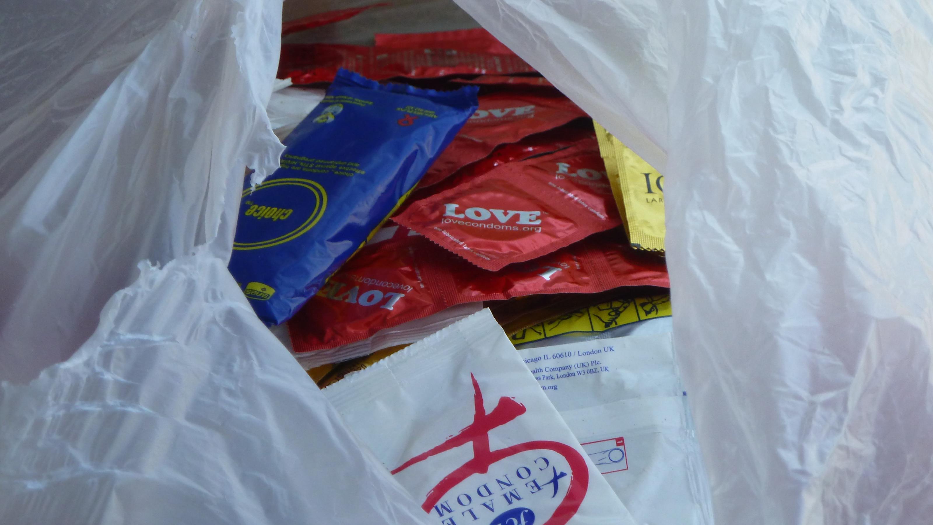 Zu sehen ist eine halb aufgerissene, weiße Tüte, in der Kondome in unterschiedlichen Verpackungen für die Verteilung bereitliegen.