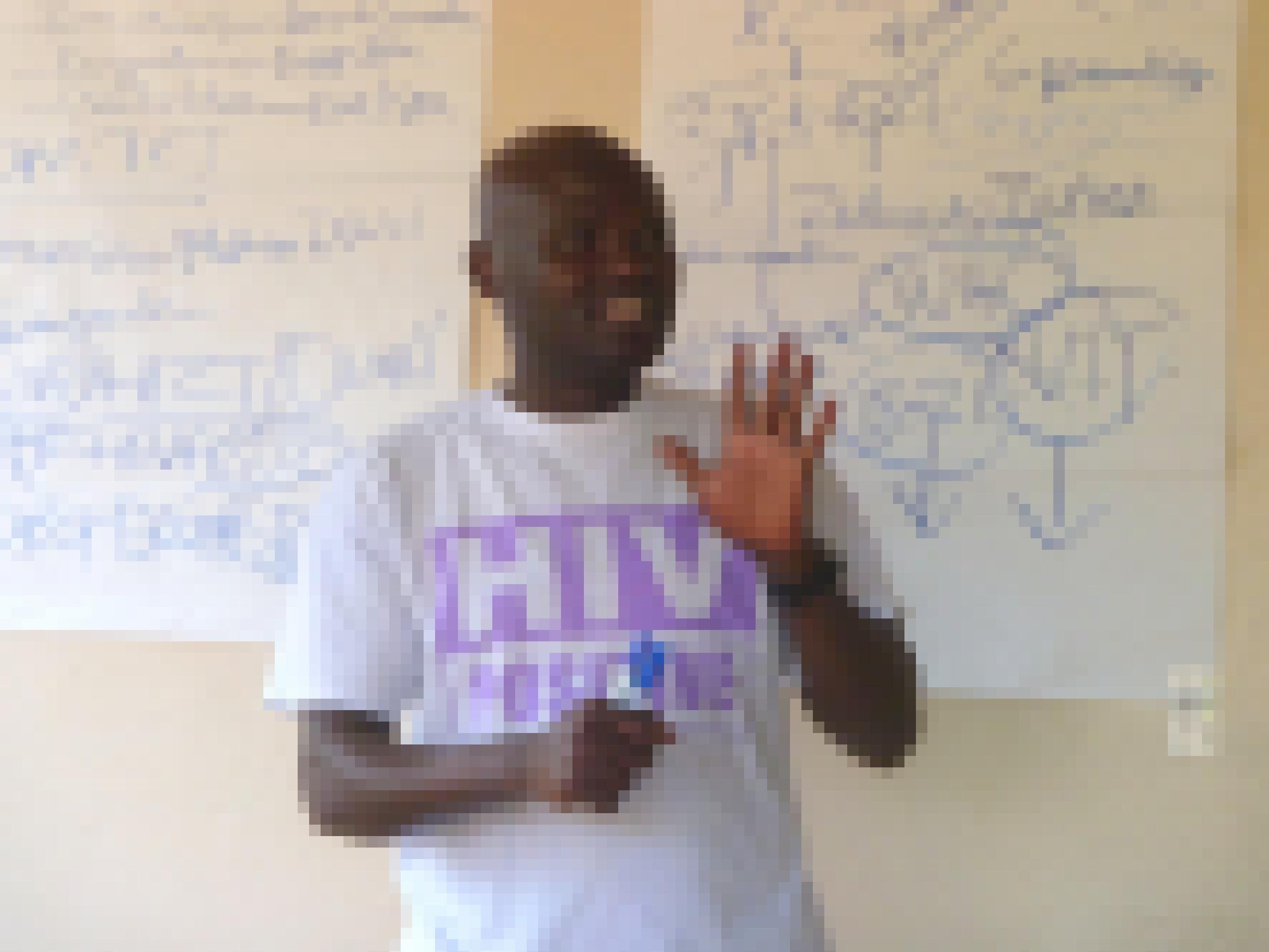 Ein Aktivist mit einem T-Shirt, der Aufdruck: HIV positiv. Er steht vor einer Tafel und gestikuliert, hält offensichtlich gerade einen Vortrag.
