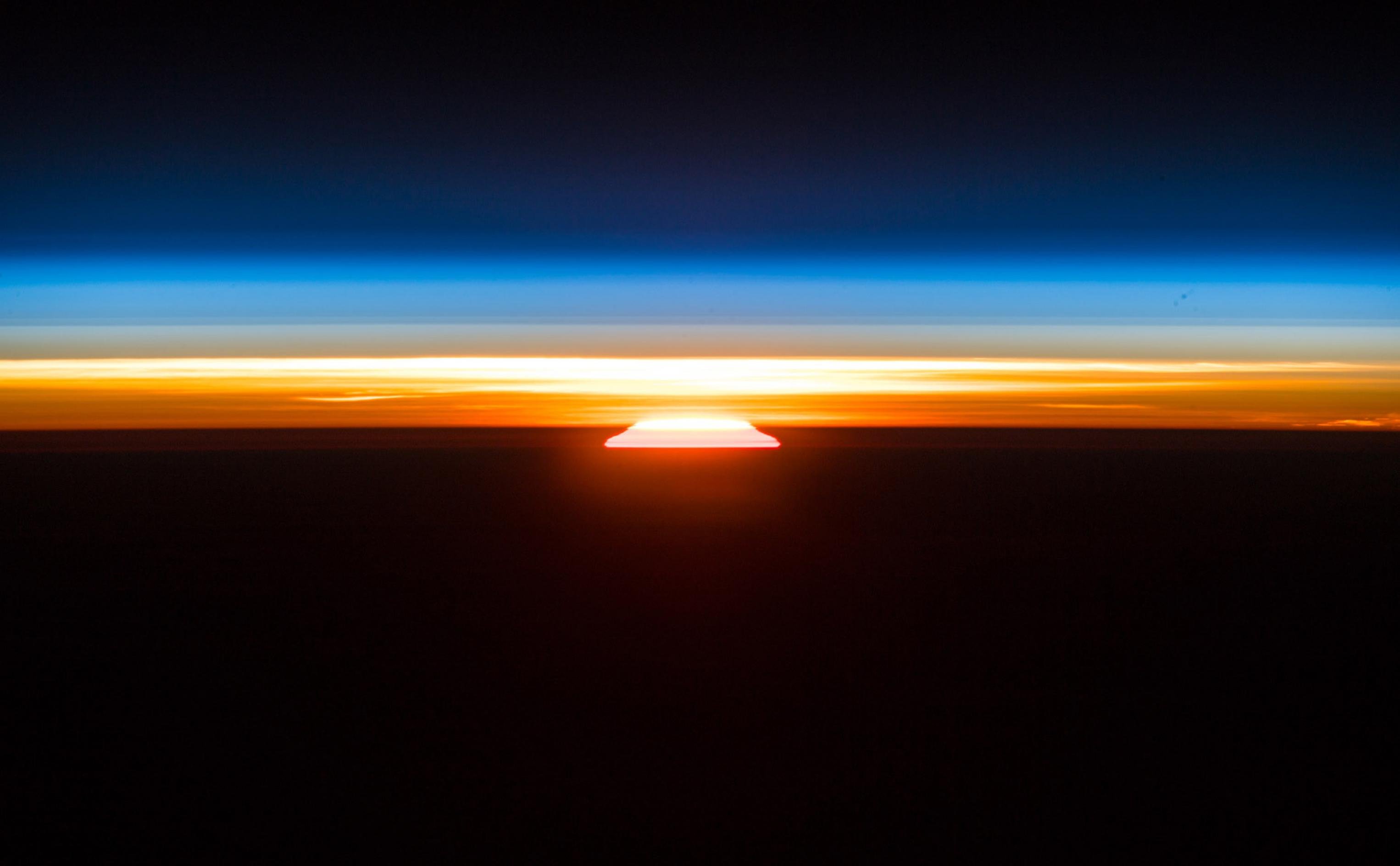 Ein Sonnenaufgang, vom Erdorbit aus vom deutschen Raumfahrer Alexander Gerst fotografiert. Über der aufgehenden Sonne die dünne, orange-blaue Erdatmosphäre, darüber die Schwärze des Weltalls.