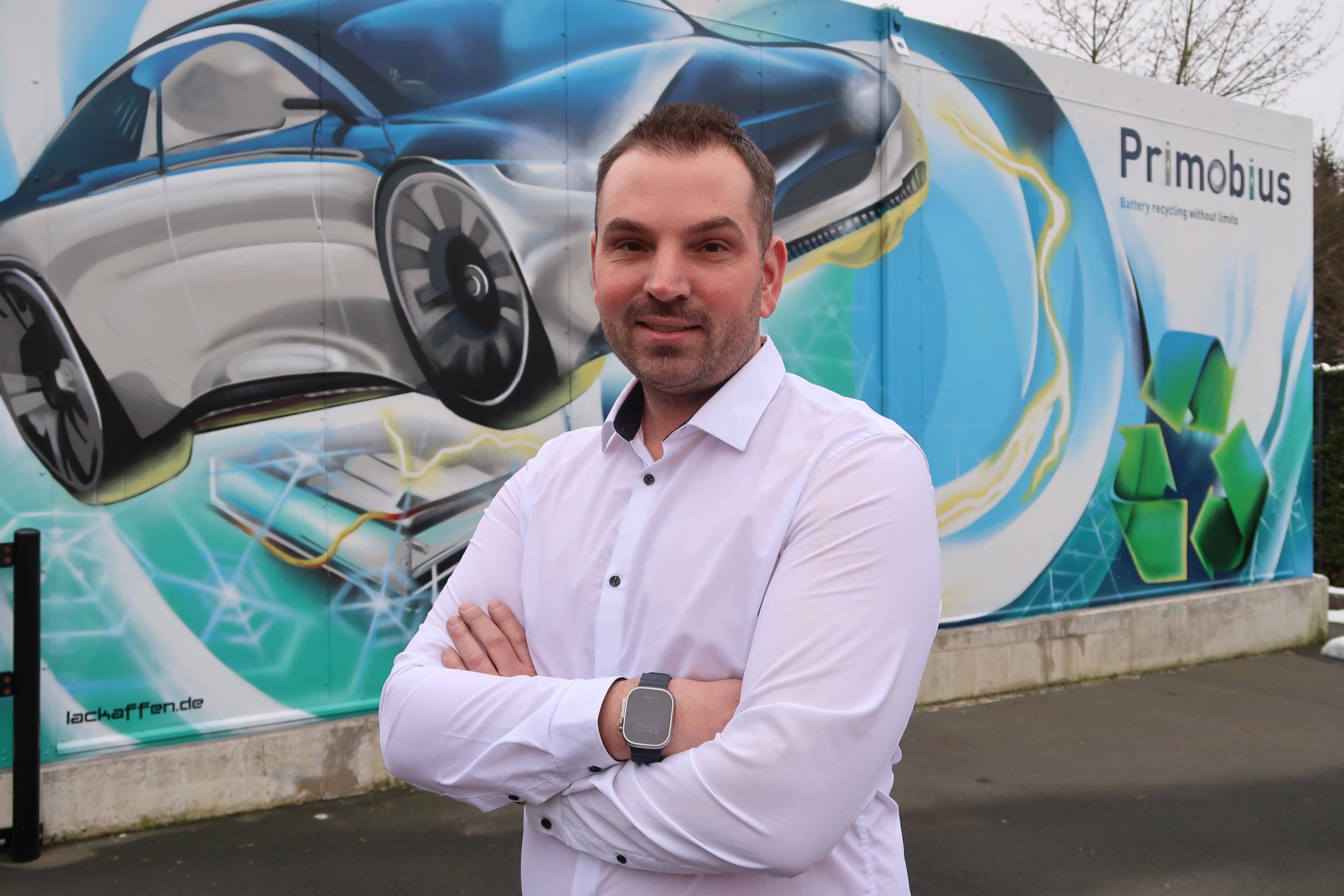 Betriebsleiter Alexander Sacherow posiert vor einem Elektroauto-Bild