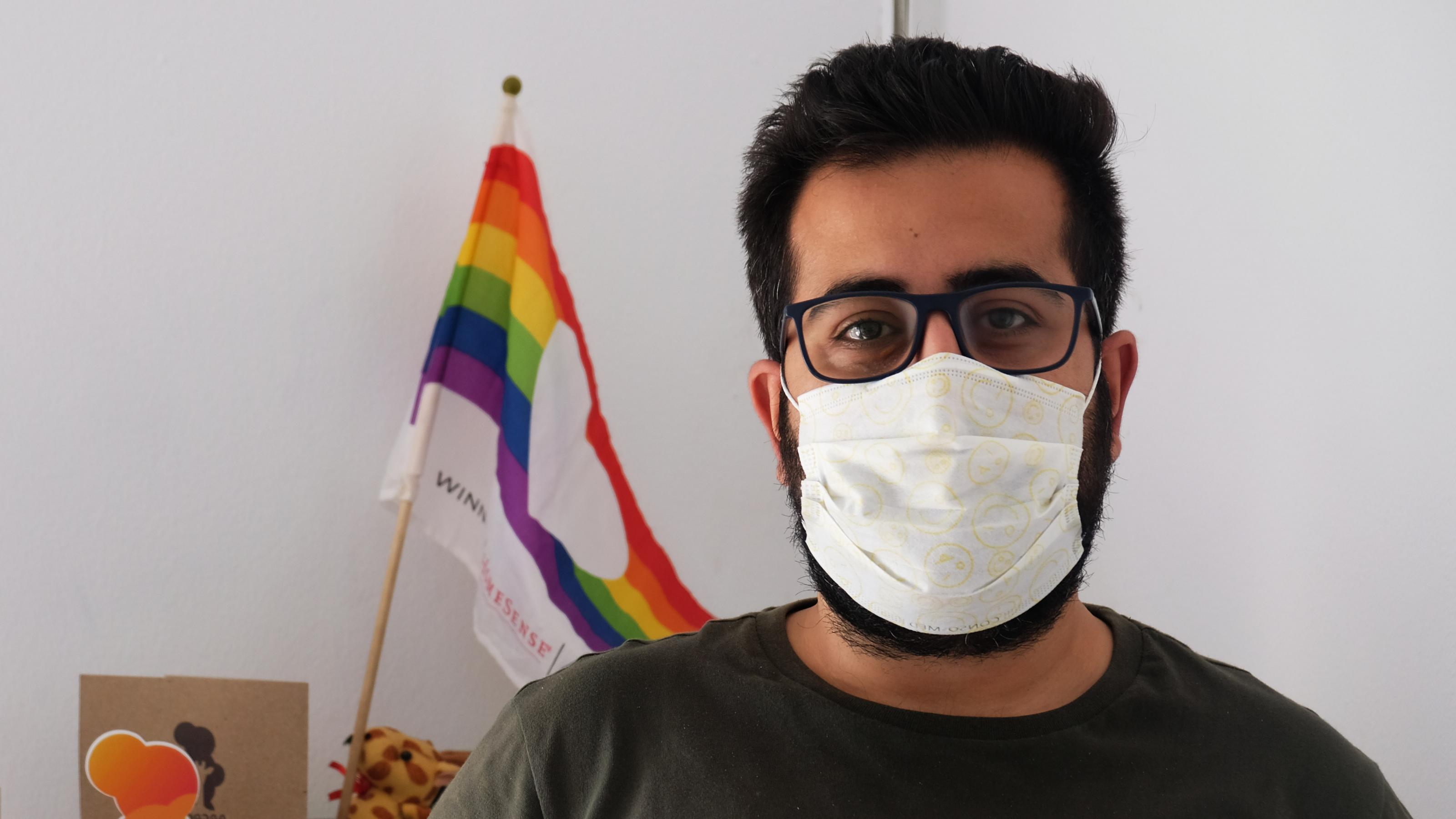 Ali Bousselmi von der tunesischen LGBTQI-Organisation steht, Maske im Gesicht, vor einer Regenbogenflagge