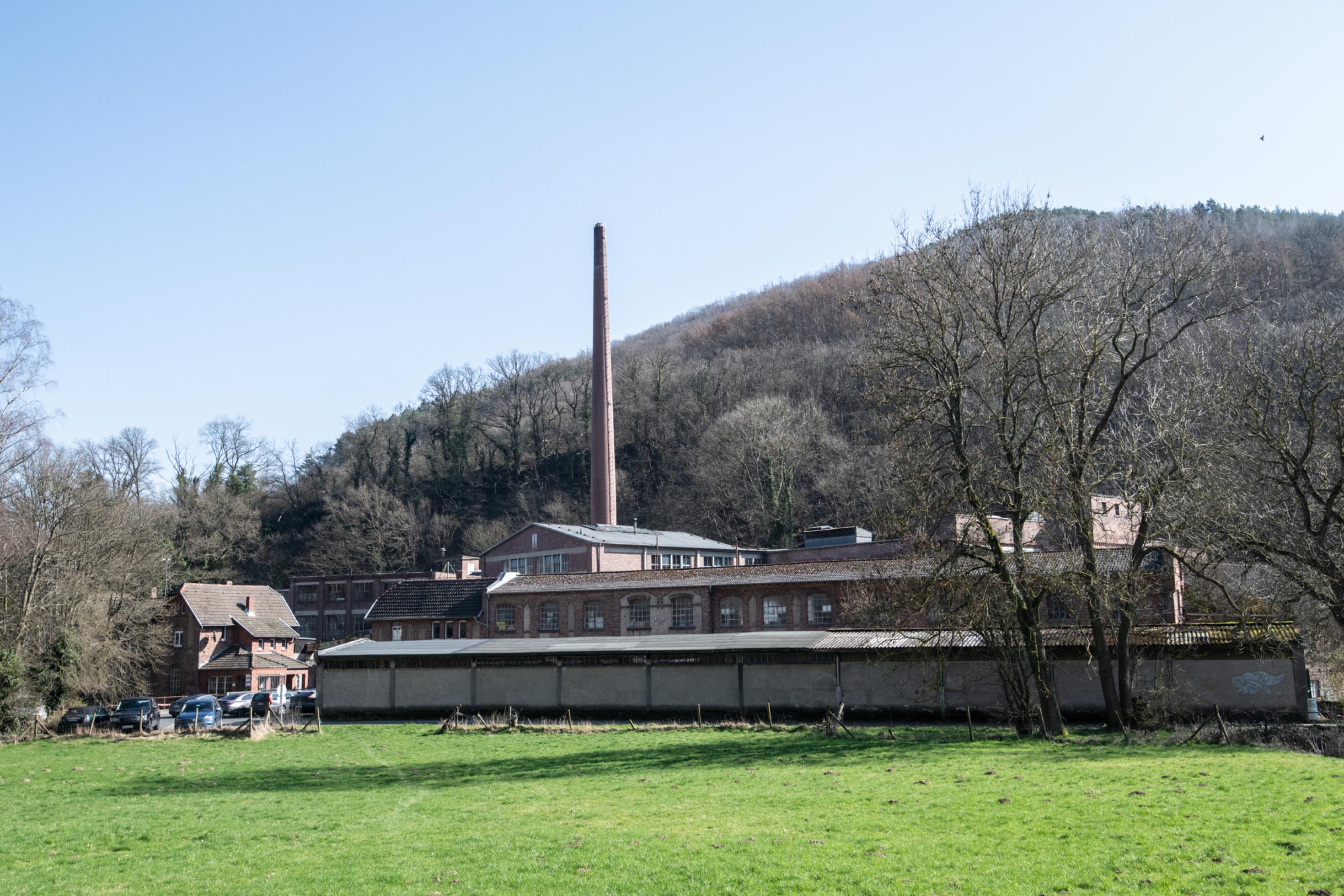 Altes Gebäude mit hohem Schornstein vor einem Hügel