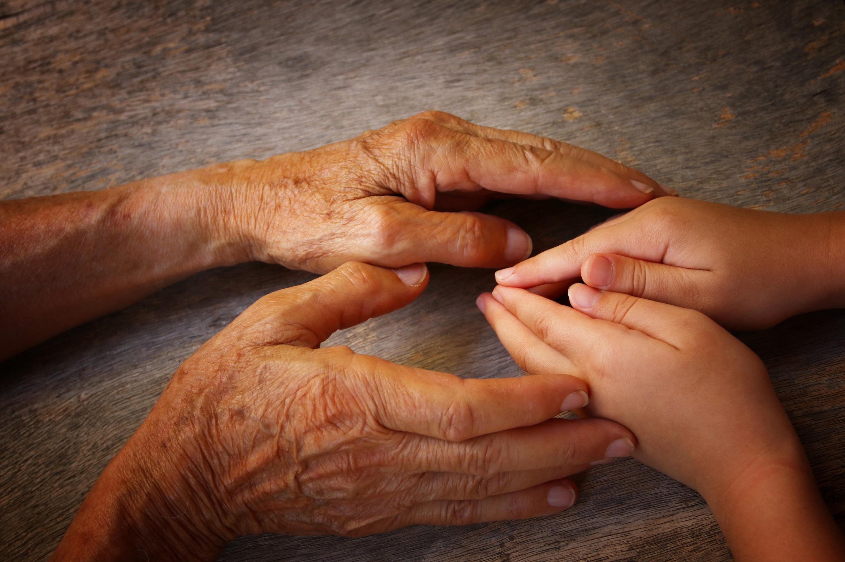 Die Hände eines alten Menschen umfassen behutsam die Hände eines Kindes.