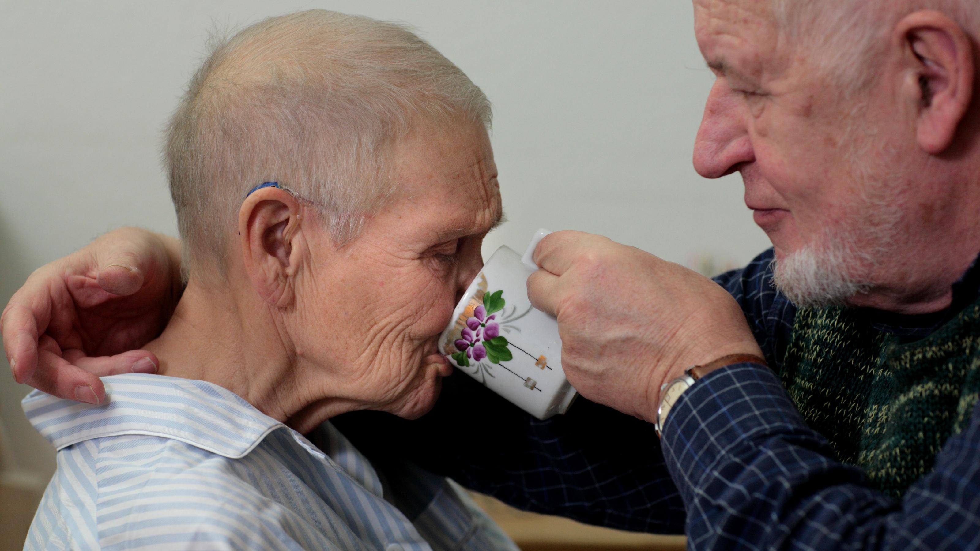 Ein alter Mann hilft seiner Frau beim Trinken, 80 Prozent der Pflegebedürftigen werden von Angehörigen versorgt.