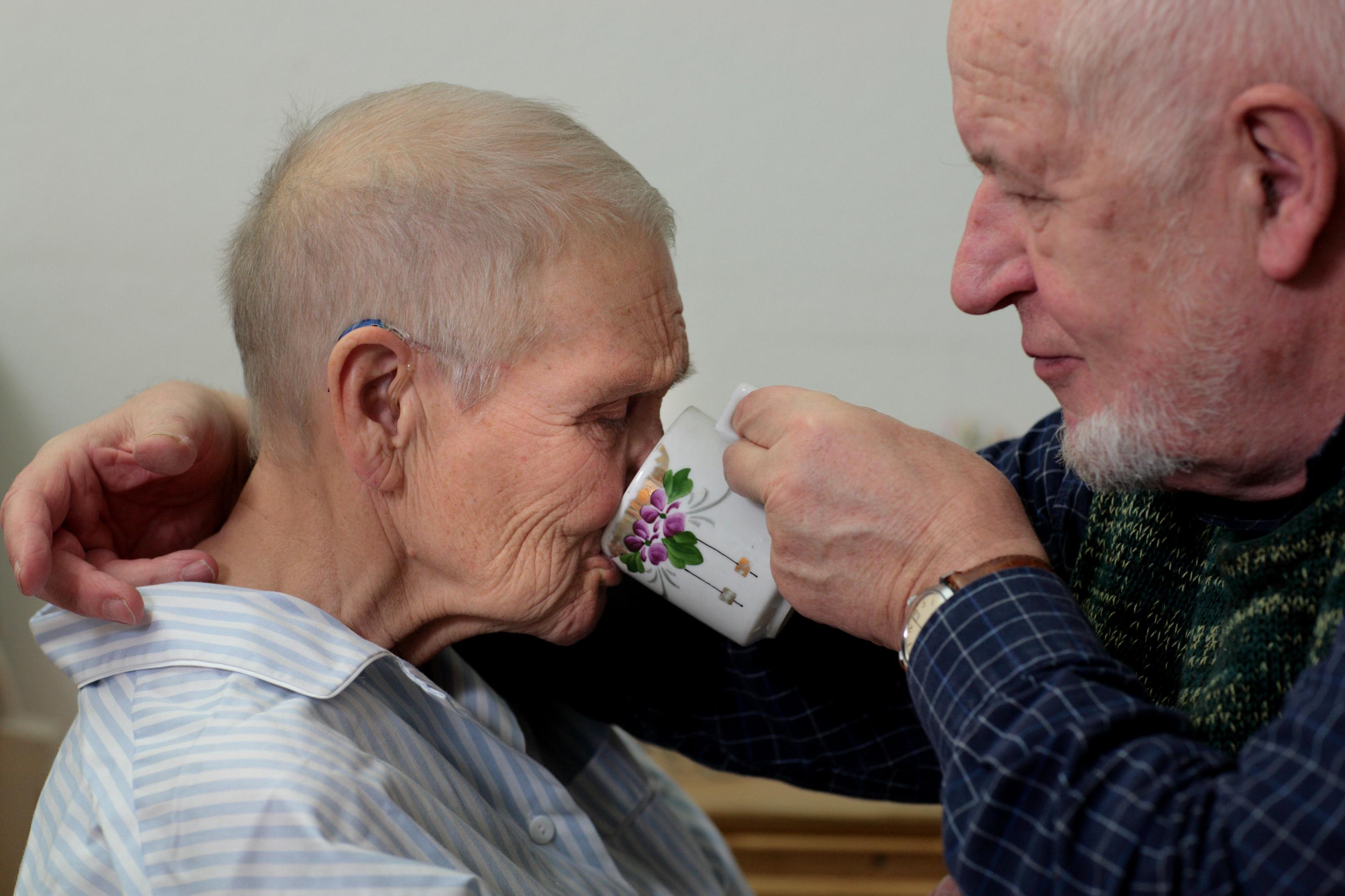 Ein alter Mann hilft seiner Frau beim Trinken, 80 Prozent der Pflegebedürftigen werden von Angehörigen versorgt.