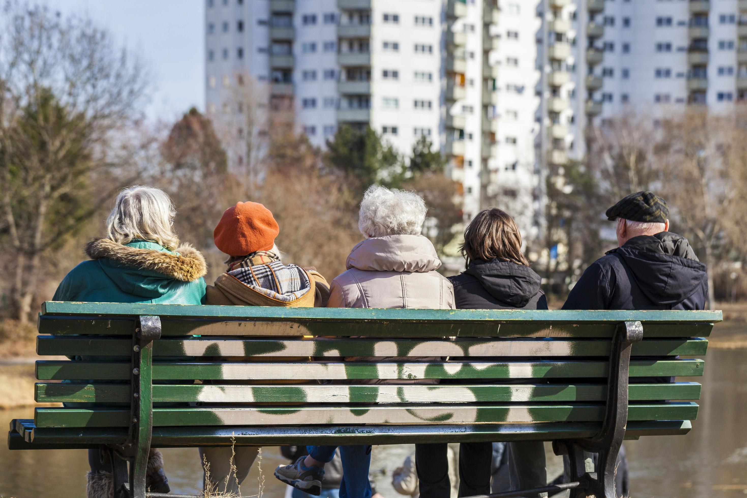 Alte Menschen sitzen auf einer Parkbank, im Hintergrund ist ein Hochhaus zu sehen. Die Gesellschaft wird älter, damit werden künftig mehr Menschen auf Pflege angewiesen sein. Doch schon heute deckt die Pflegeversicherung Pflegekosten nicht mehr ausreichend ab.