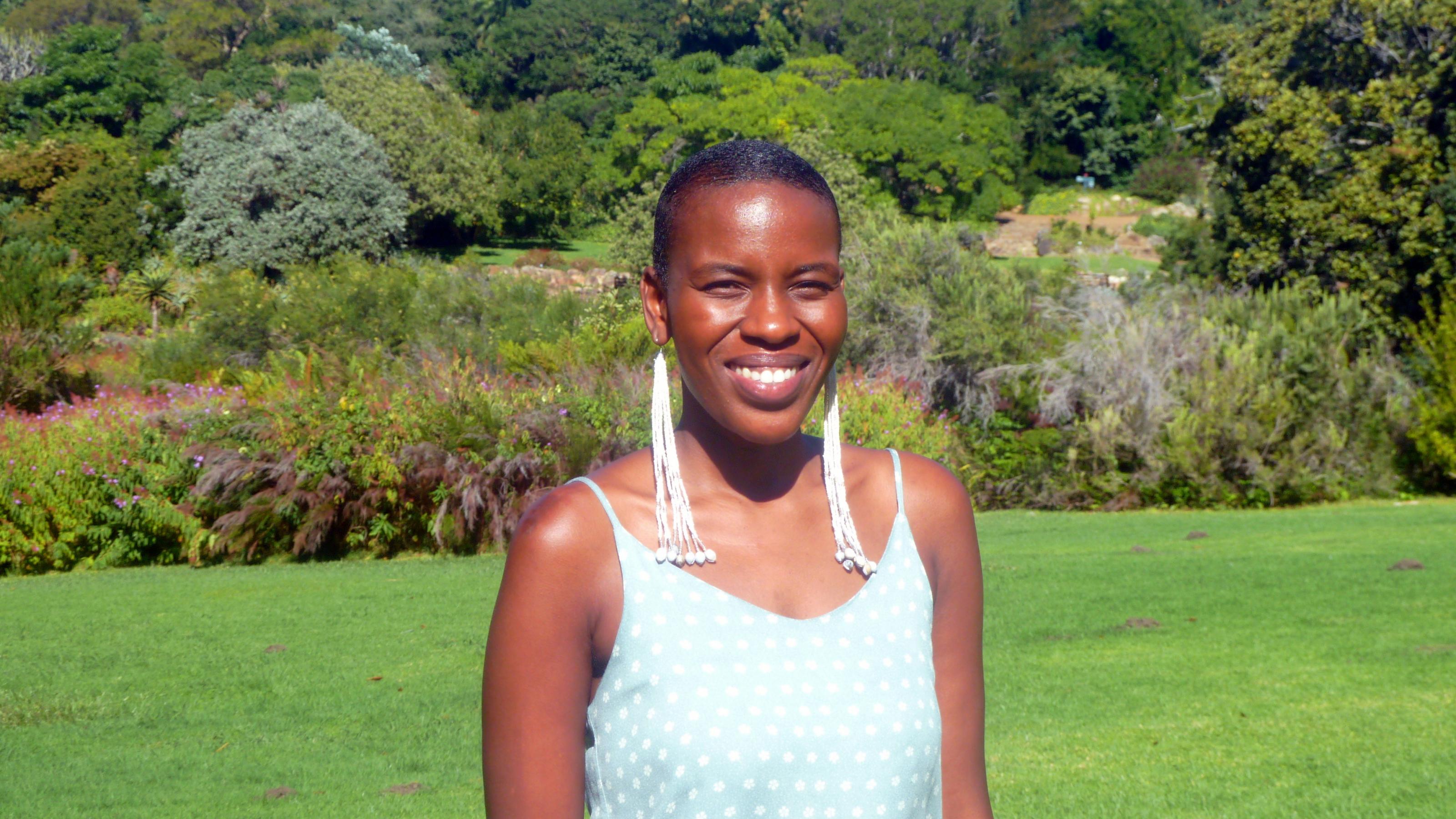 Die Anwältin lächelt im Botanischen Garten in Kapstadt in die Kamera, sie trägt ein sportliches, schulterloses Top