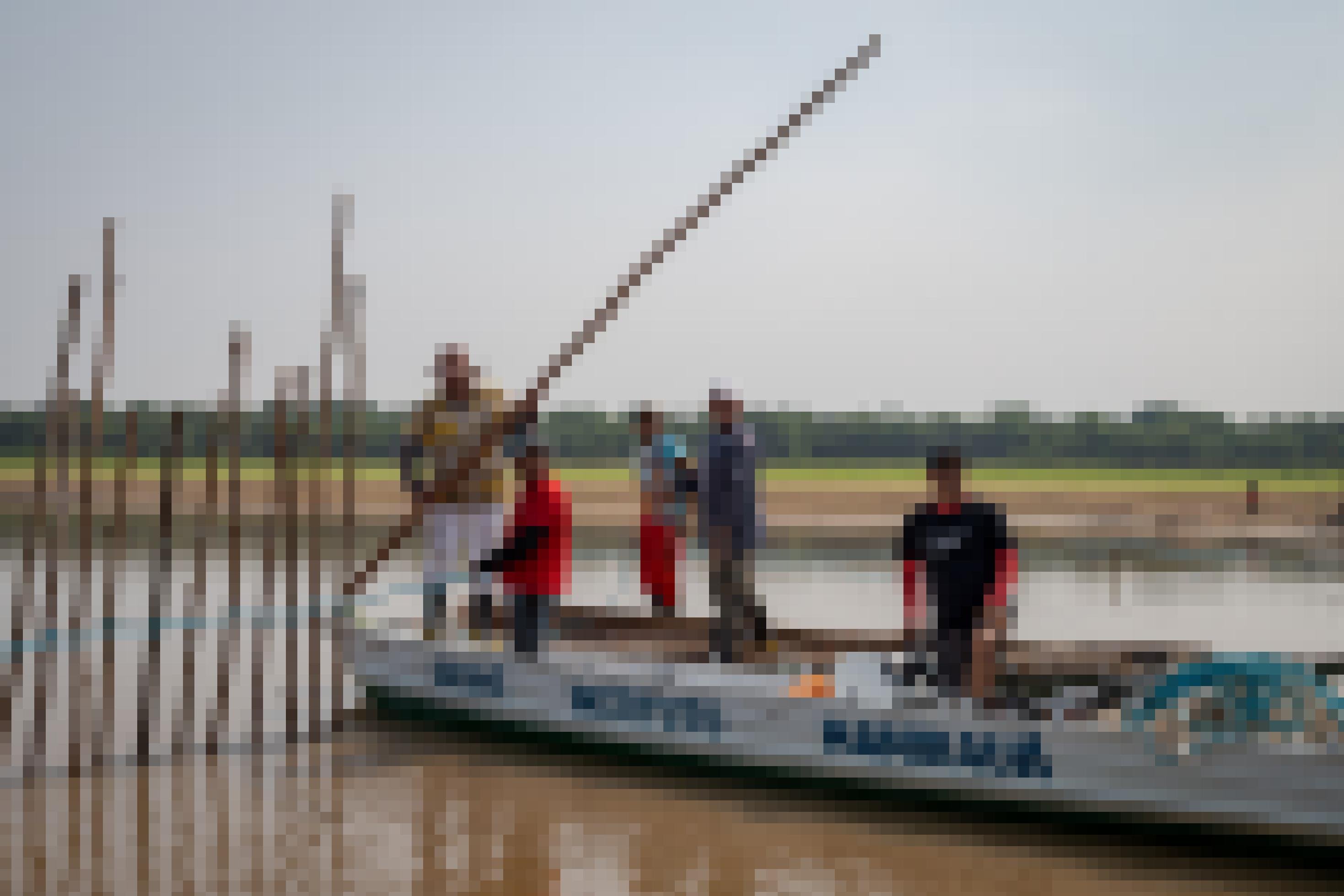 Fünf Männer auf einem Boot grenzen ein Gebiet der Lagune mit Baumstecken ab