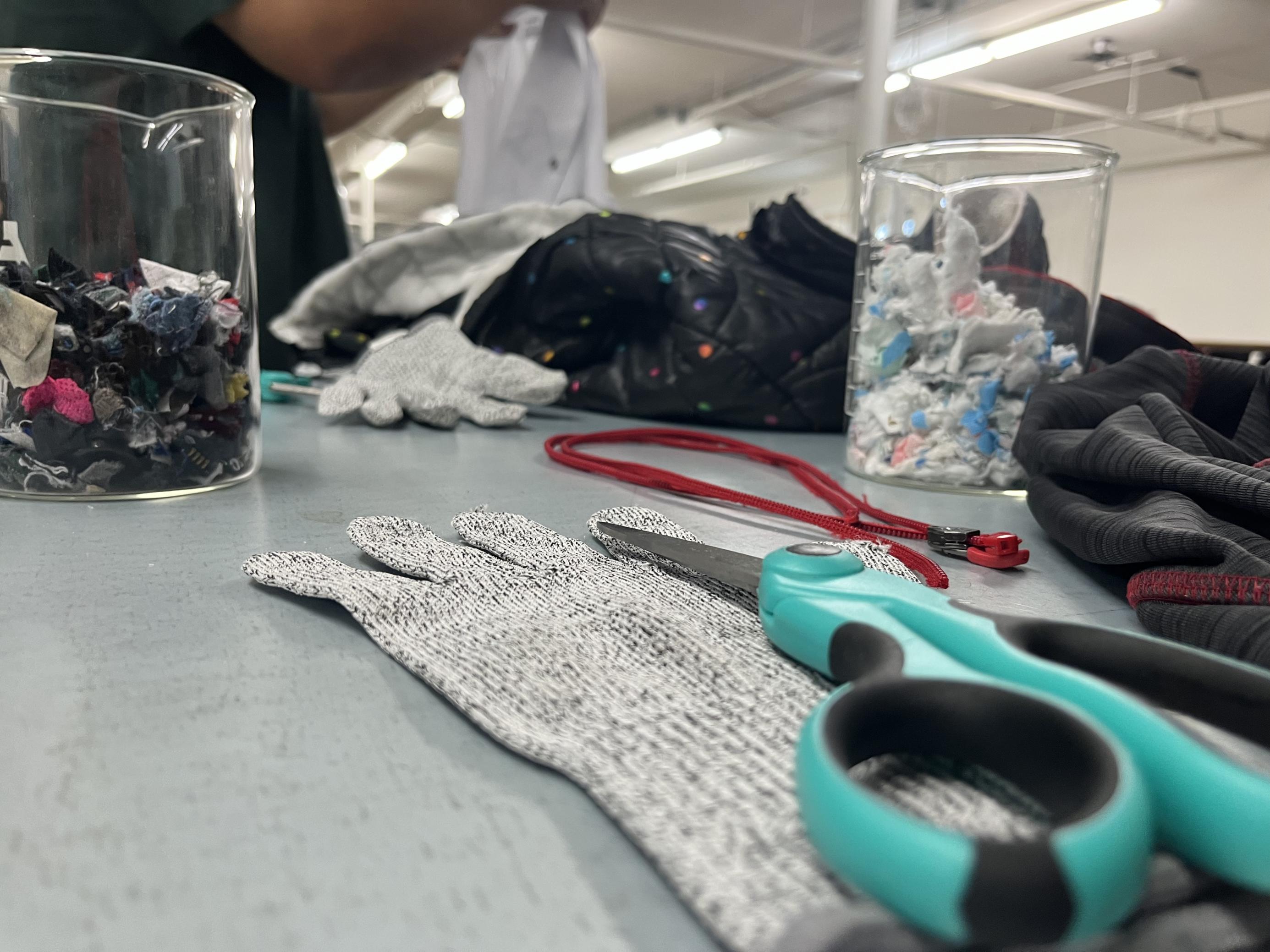 Scheren, Reissverschlüsse, Stoffetzen und ein Kleiderberg türmen sich auf einem Tisch im Ambercycle-Labor. Studierende versuchen hier, Polyester zu isolieren. Vergeblich.