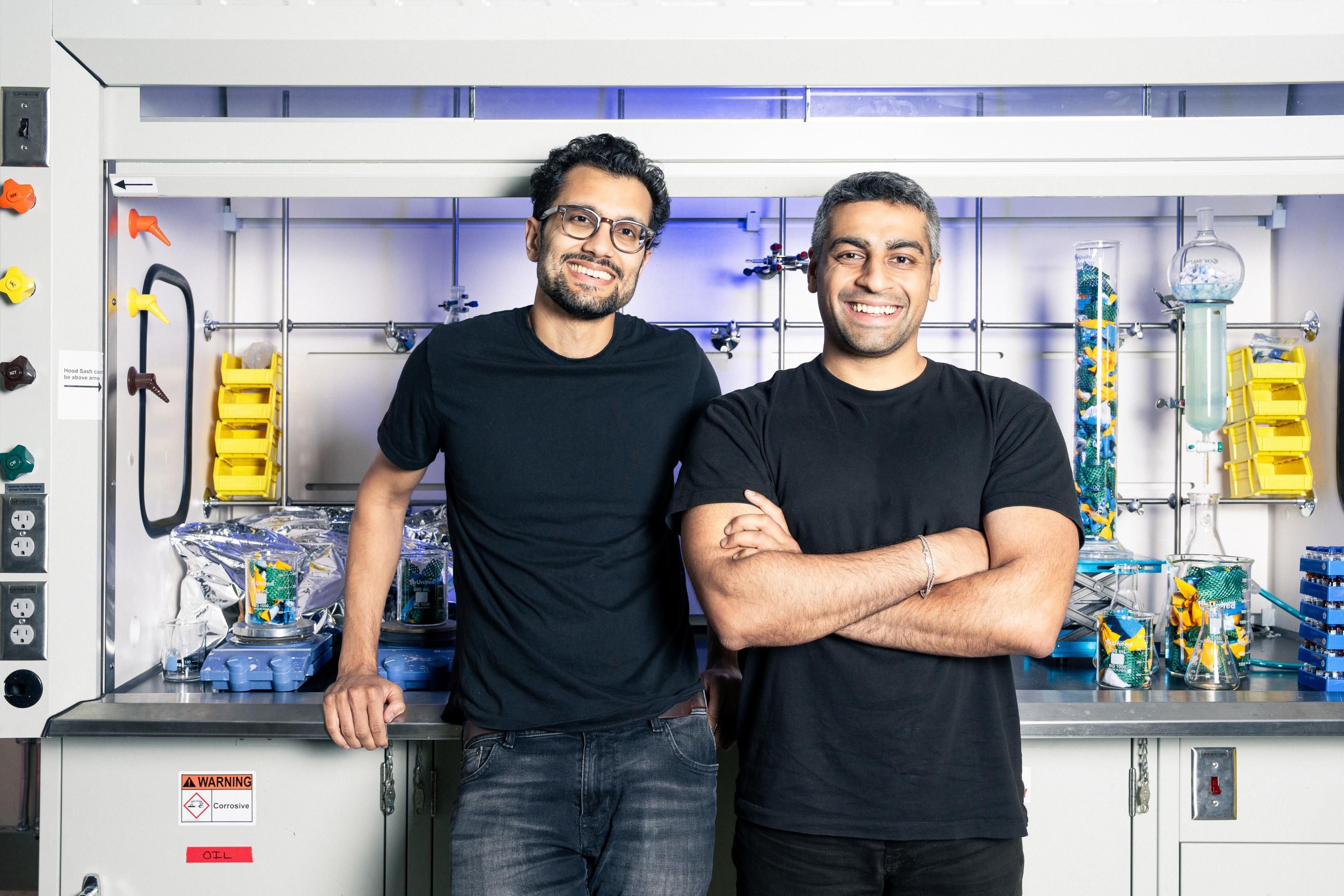Zwei Männer Mitte dreißig stehen vor einem regal mit Laborutensilien und lachen in die Kamera. Es sind die Ambercycle-Gründer Shay Sethi und Moby Ahmed.