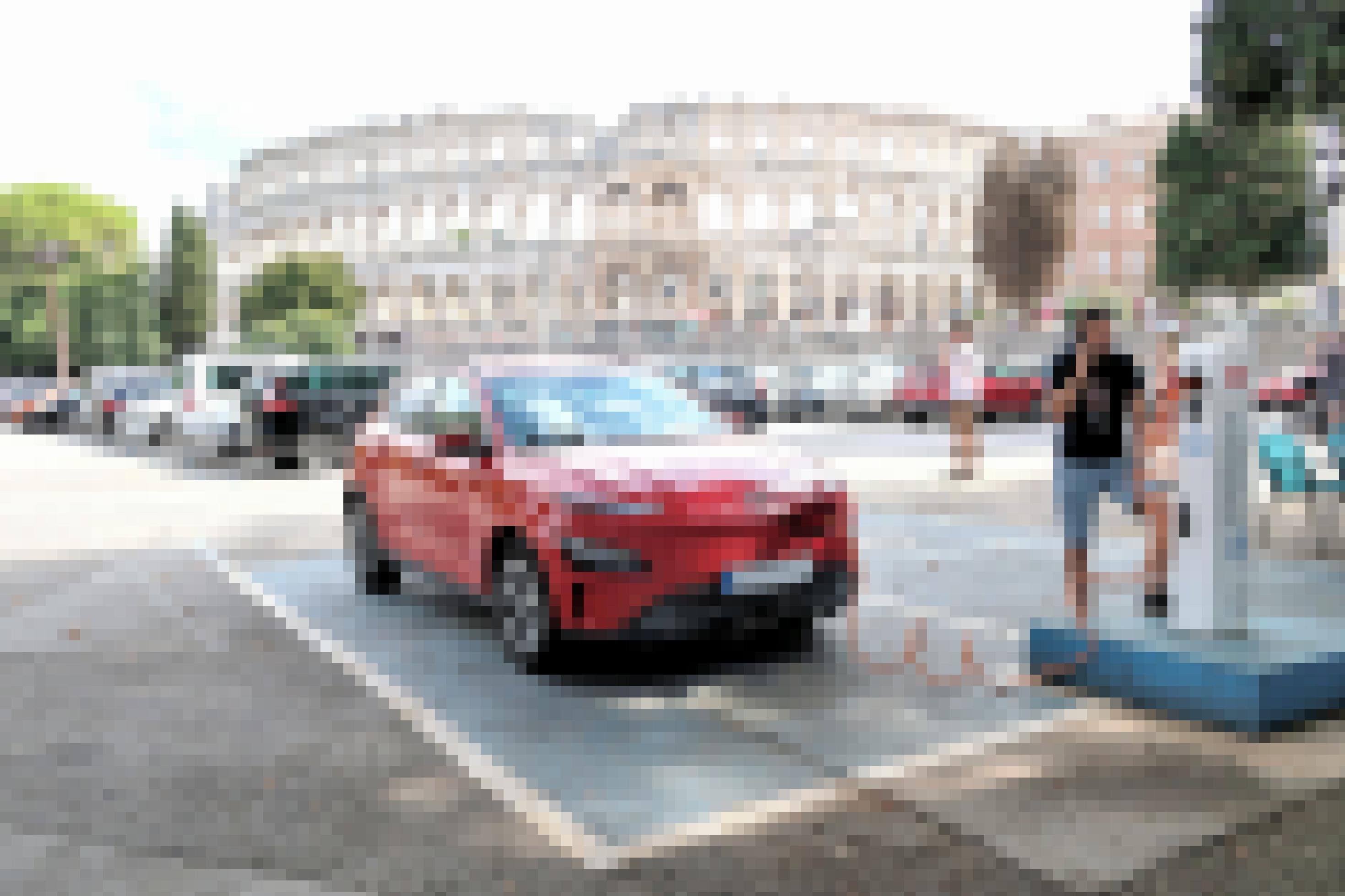 Ein Elektroauto steht auf einem Parkplatz und ist mit einer Ladestation verbunden. Im Hintergrund ist ein römisches Amphi-Theater zu sehen.