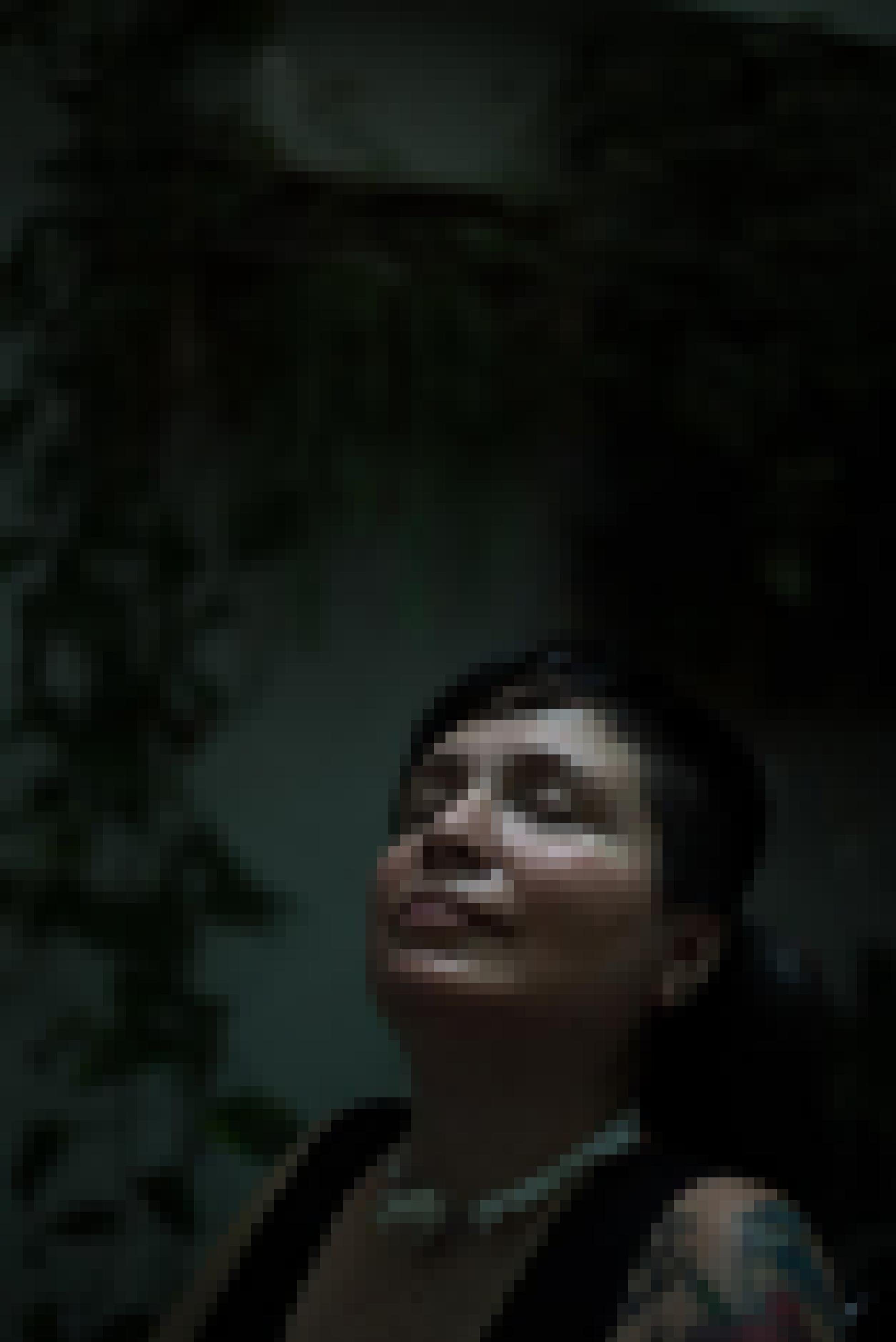 Gesicht einer Frau mit kurzen dunklen Haaren und geschlossenen Augen, nach oben gestreckt. Dunkler Hintergrund