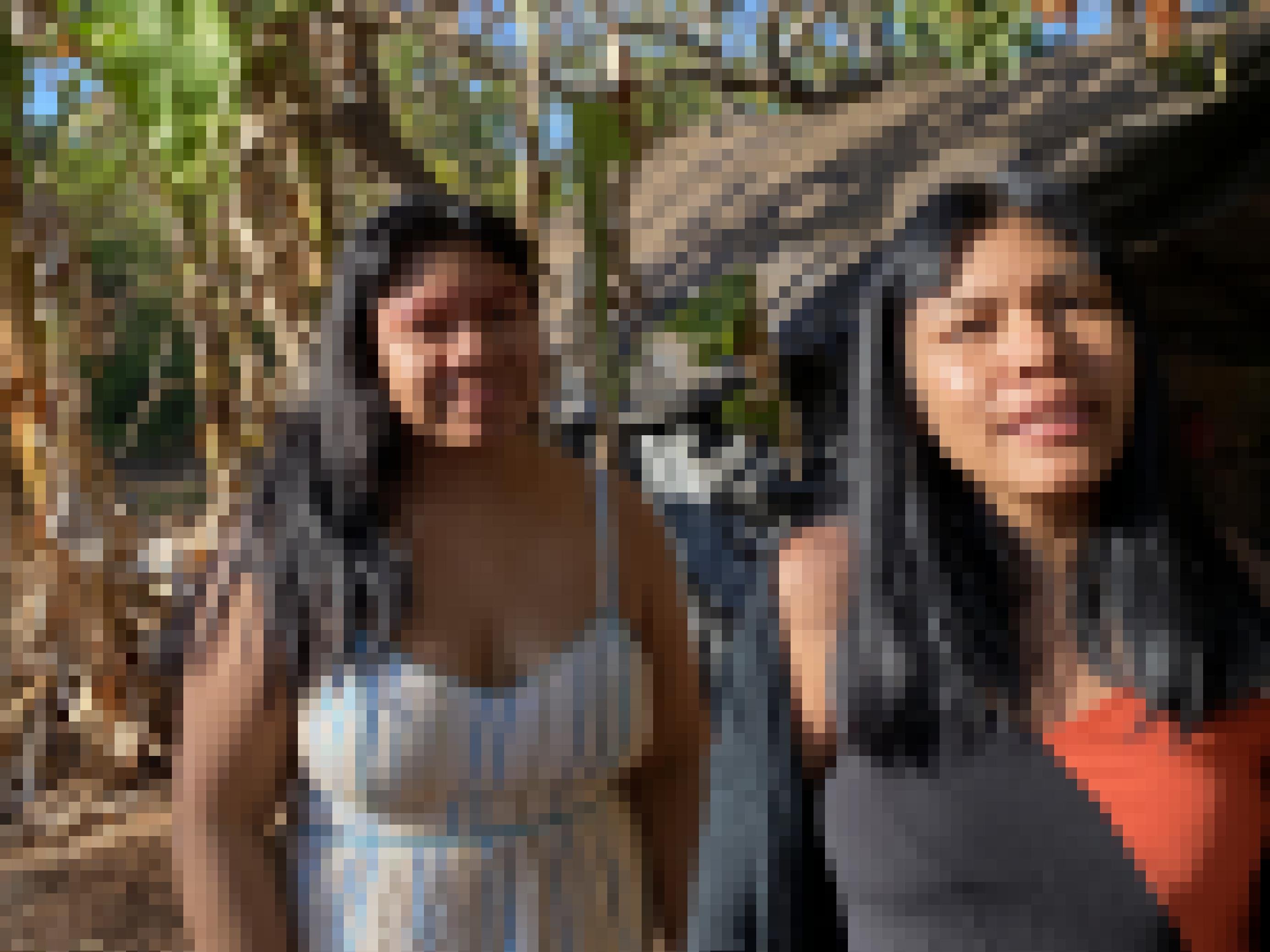 Zwei Frauen mit langen schwarzen Haaren vor Bananenstauden und einem mit Plastikfolie gedeckten Haus.