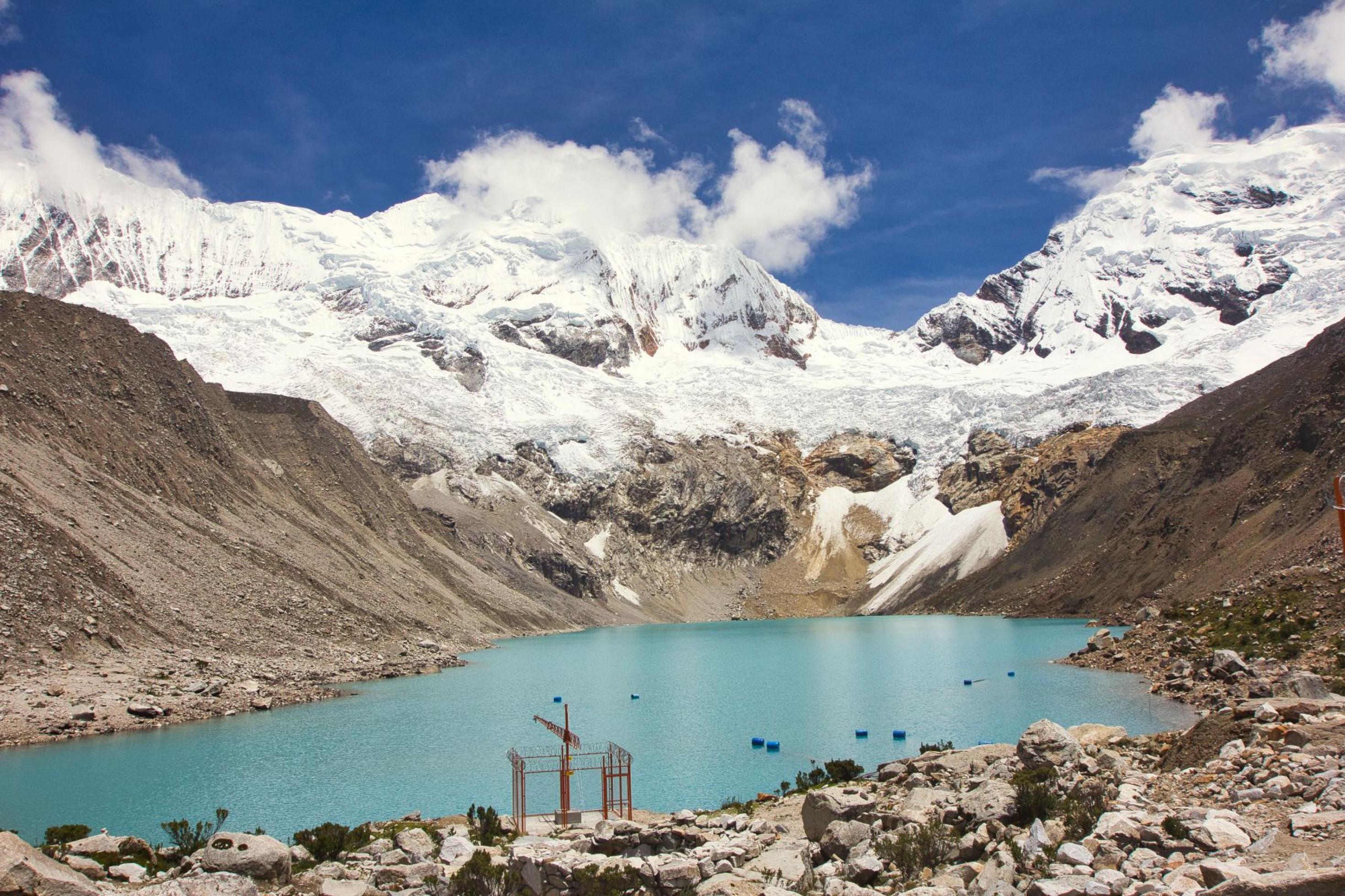 Berglandschaft, im Hintergrund schneebedeckte Gipfel, im Vordergrund ein ovaler See mit blauem Wasser, eingesäumt von Bergen.
