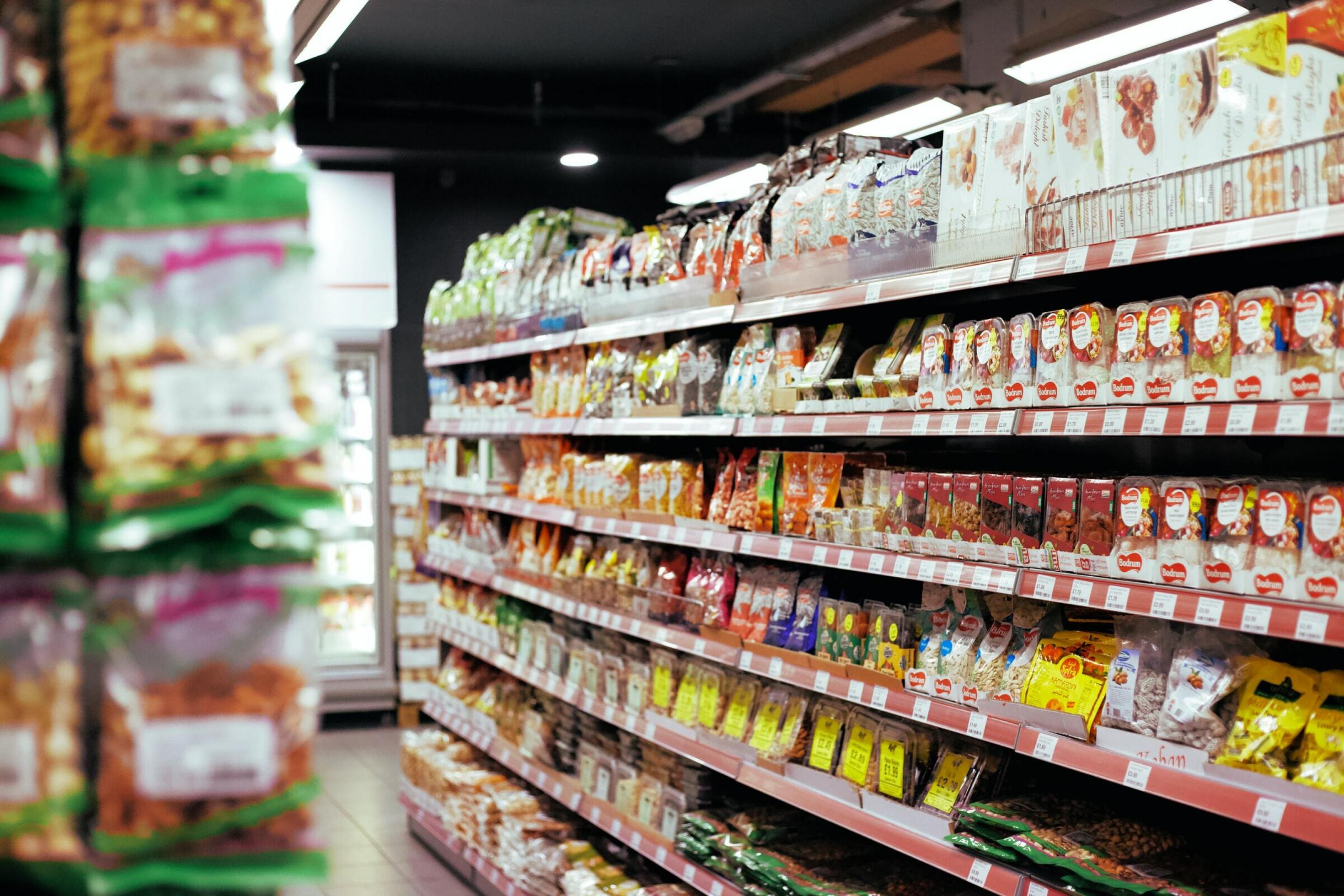 Viele bunte Lebensmittel-Verpackungen stehen in einem Regal in einem Supermarkt.