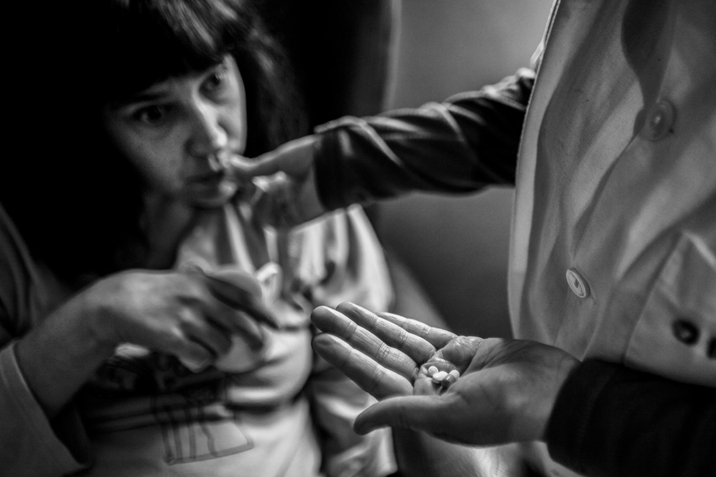 Das schwarz-weiß-Bild zeigt die Frau Encardi. Sie bekommt von einer Pflegekraft Medikamente gereicht. Encardi wird von ihrem Mann Alejandro zu Hause gepflegt. In Spanien wurden 2007 die Hilfen im Pflegebereich drastisch gekürzt.