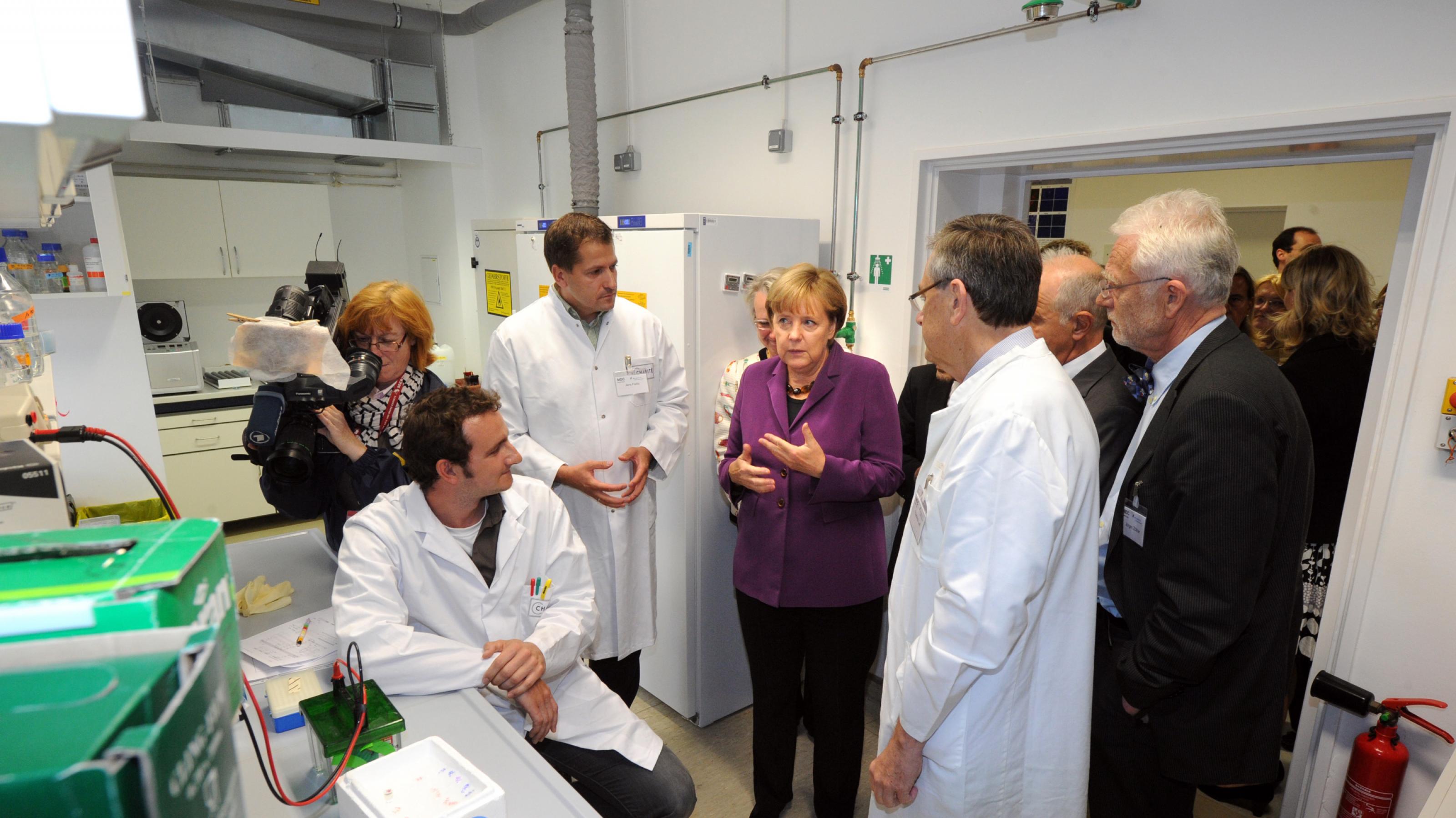 Angela Merkel steht mit Mitarbeitern in einem Labor.