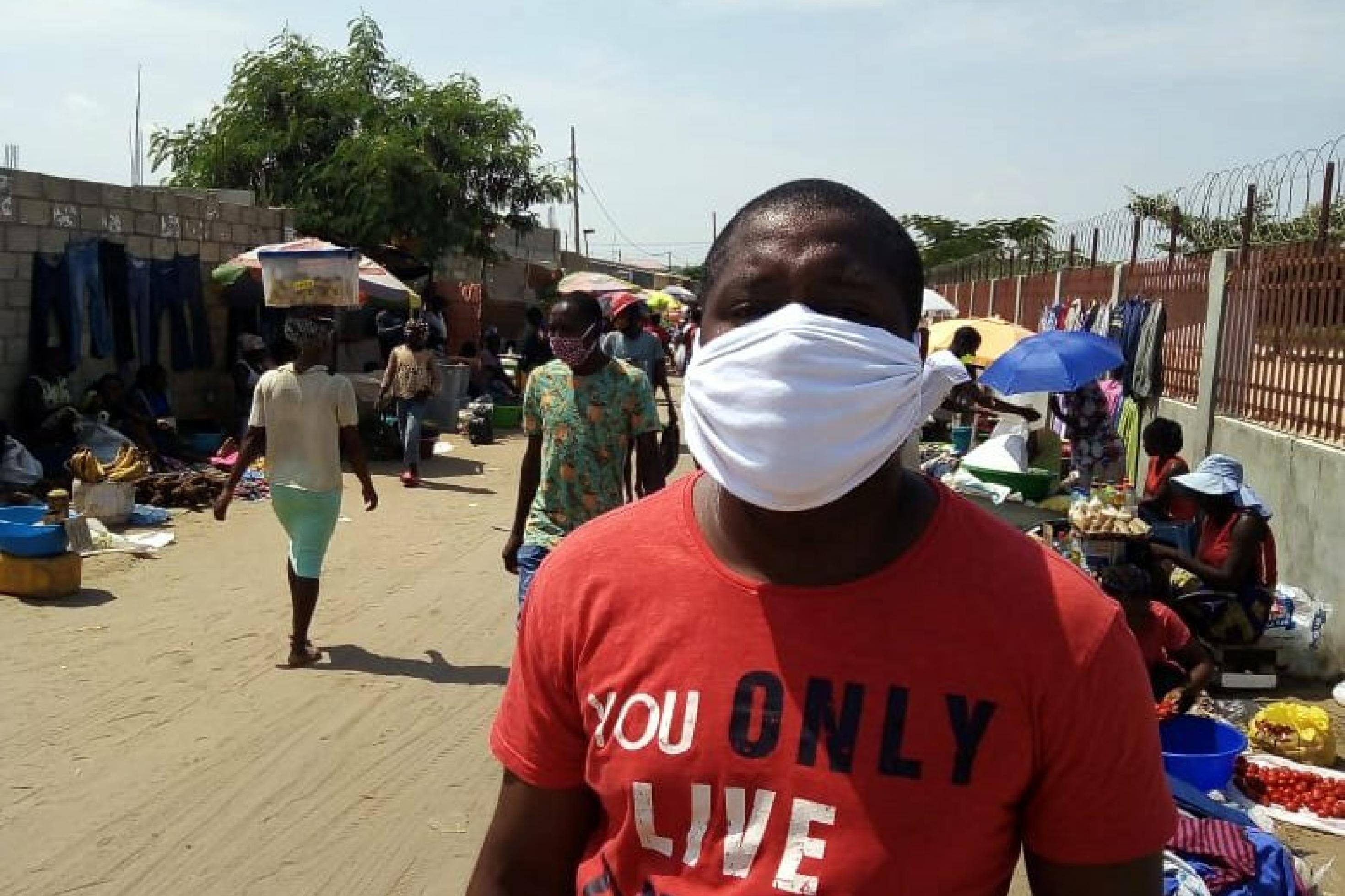 ein Angolaner namens Caius César auf einem Markt in Luanda, er trägt eine Gesichtsmaske