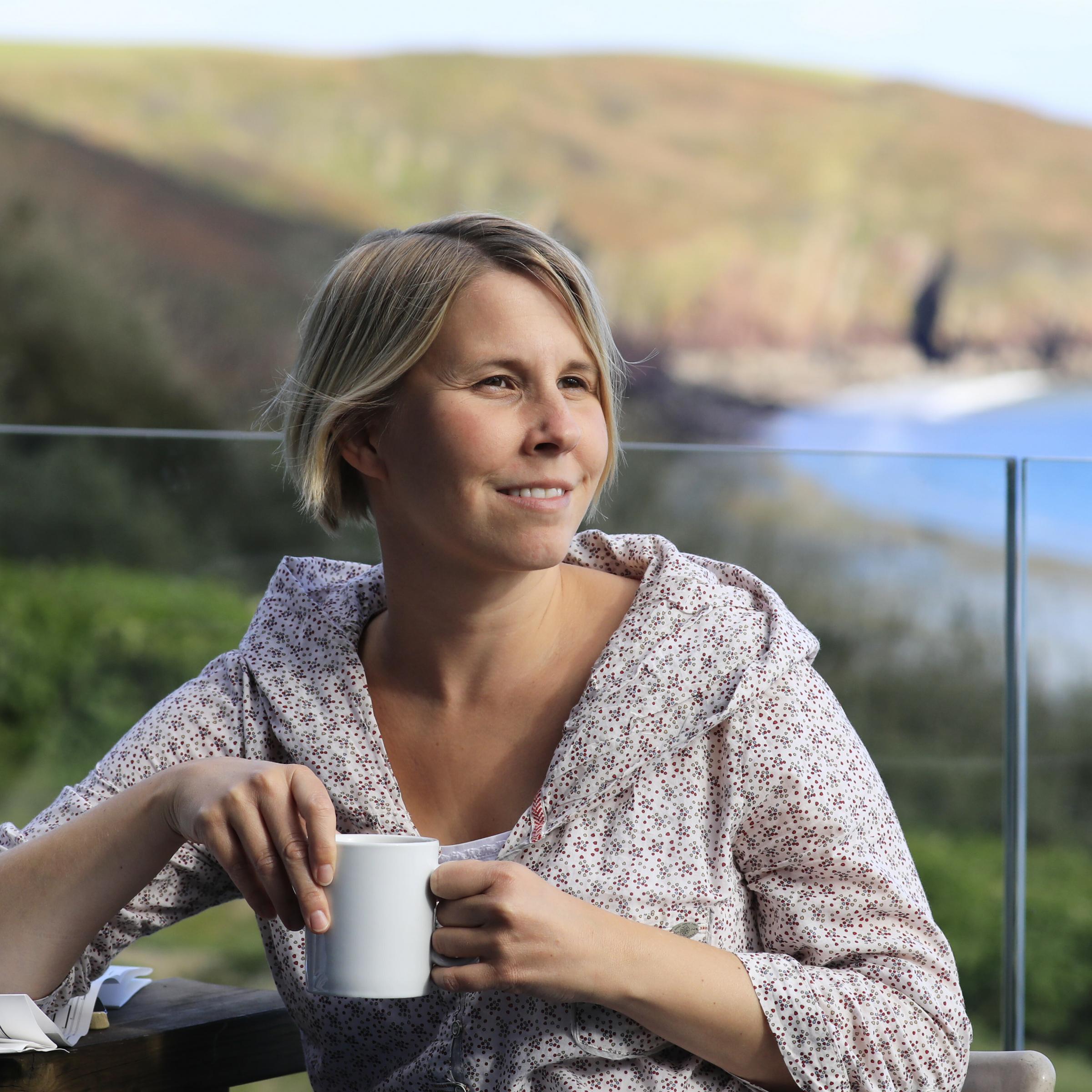 Anne Preger sitzt mit einem Becher in der Hand auf einer Terrasse.