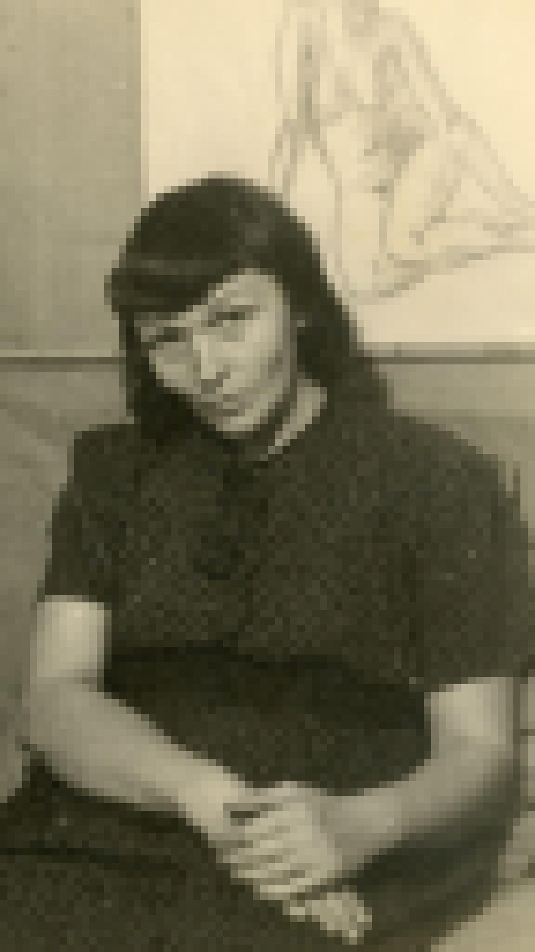 Eine brünette Frau sitzt im Eck eines Zimmers, das mit groben Leinwandstoff ausgekleidet ist und blickt in die Kamera.