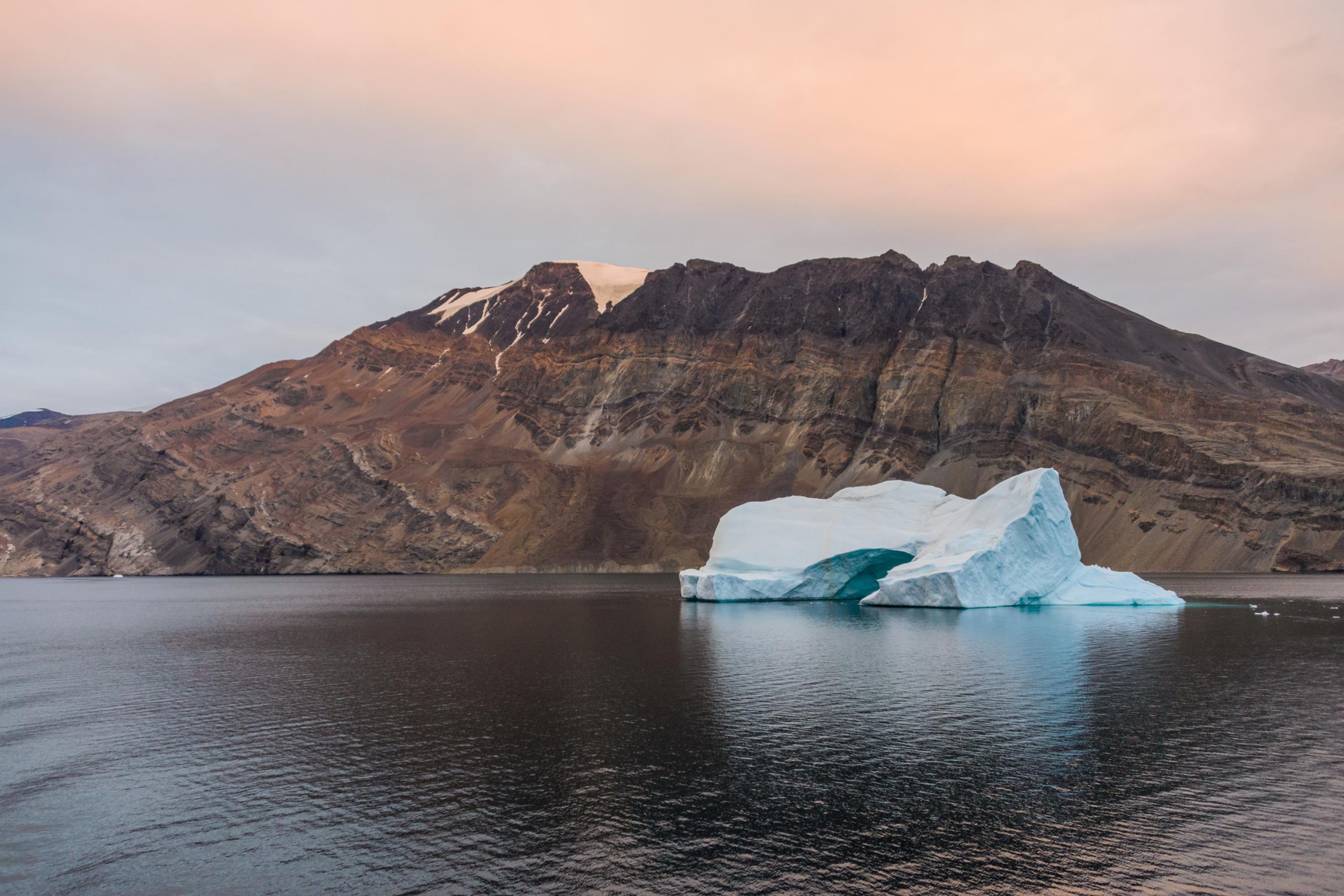 Das Bild zeigt eine grönländische Gebirgslandschaft, mit einem See und einem kleinen Eisberg im Vordergrund.