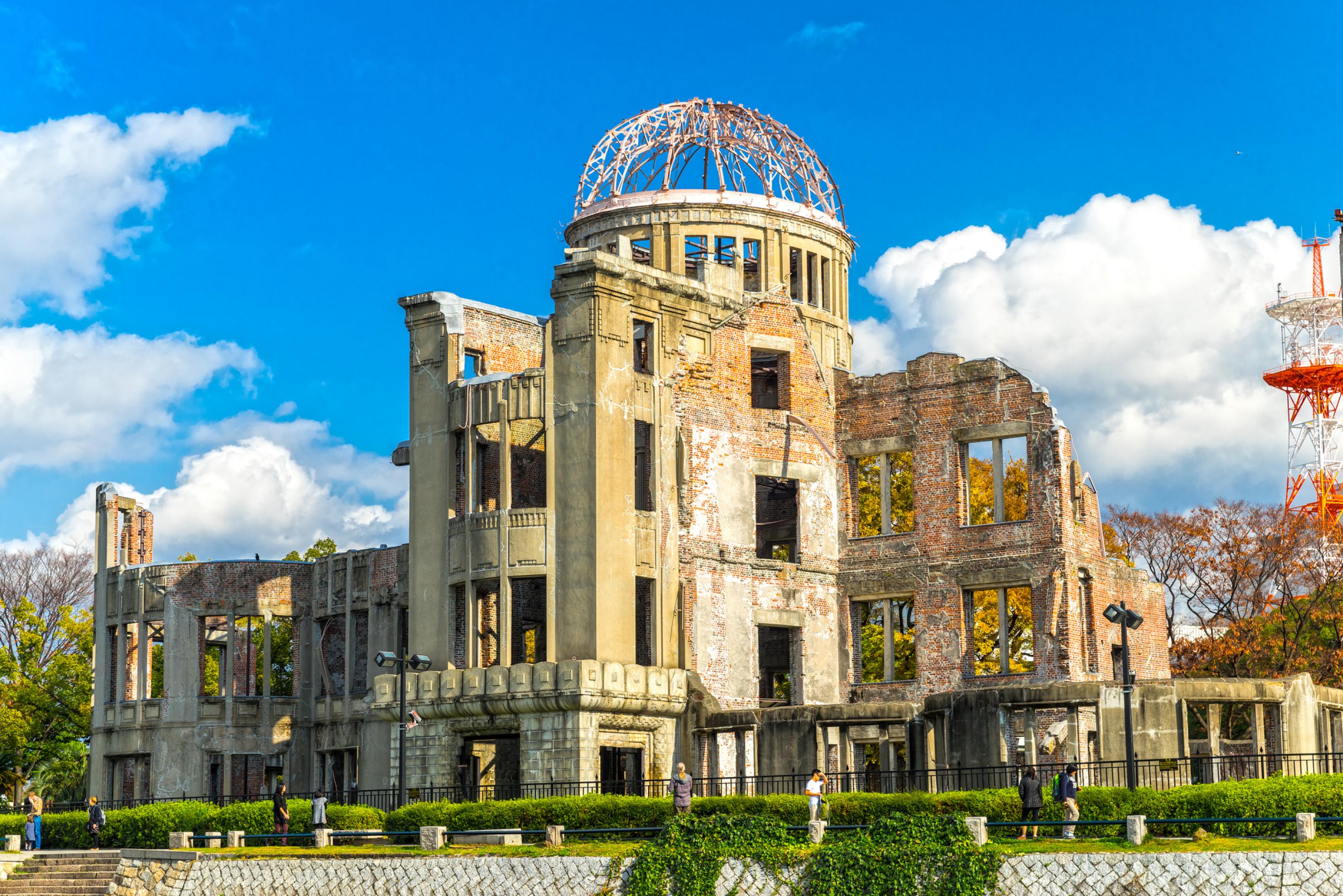 Das Bild zeigt das Friedensdenkmal von Hiroshima, ein von der Atombombe zerstörtes Gebäude mit einem Eisengerippe als Dach im Zentrum der Stadt.