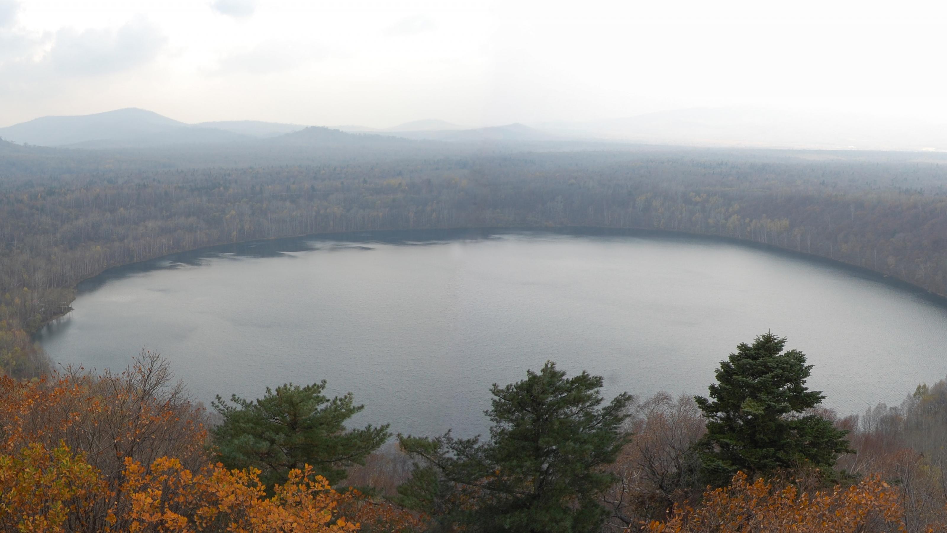 Großer runder See, ein Vulkankrater, umgeben von Wald und Hügeln.