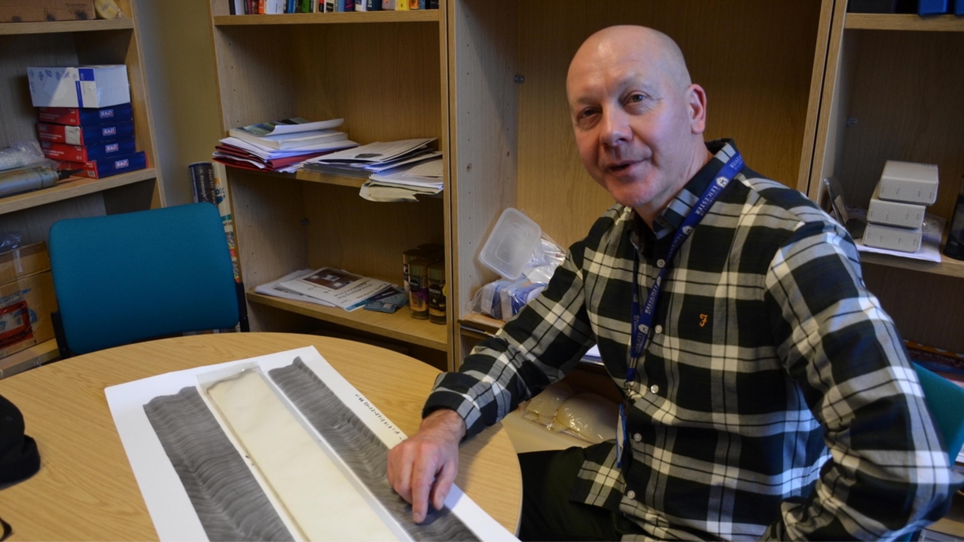 Mittelalter Mann mit Glatze in Büro mit geologischen Bohrproben auf dem Tisch.