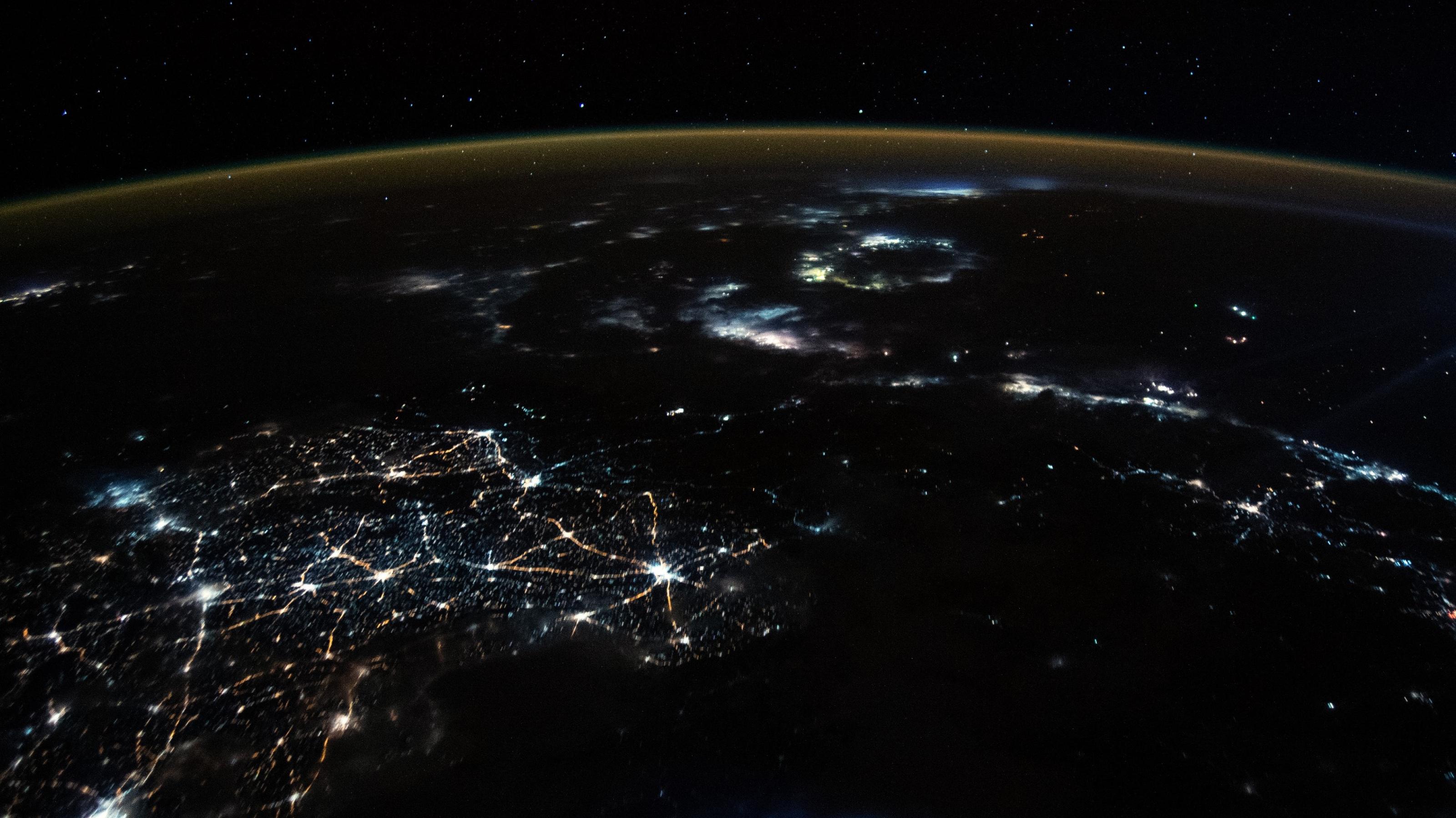 Blick aus der Internationalen Raumstation auf den nachtschwarzen Planeten mit vielen Lichtern aus Städten und von Fischereiaktivität.