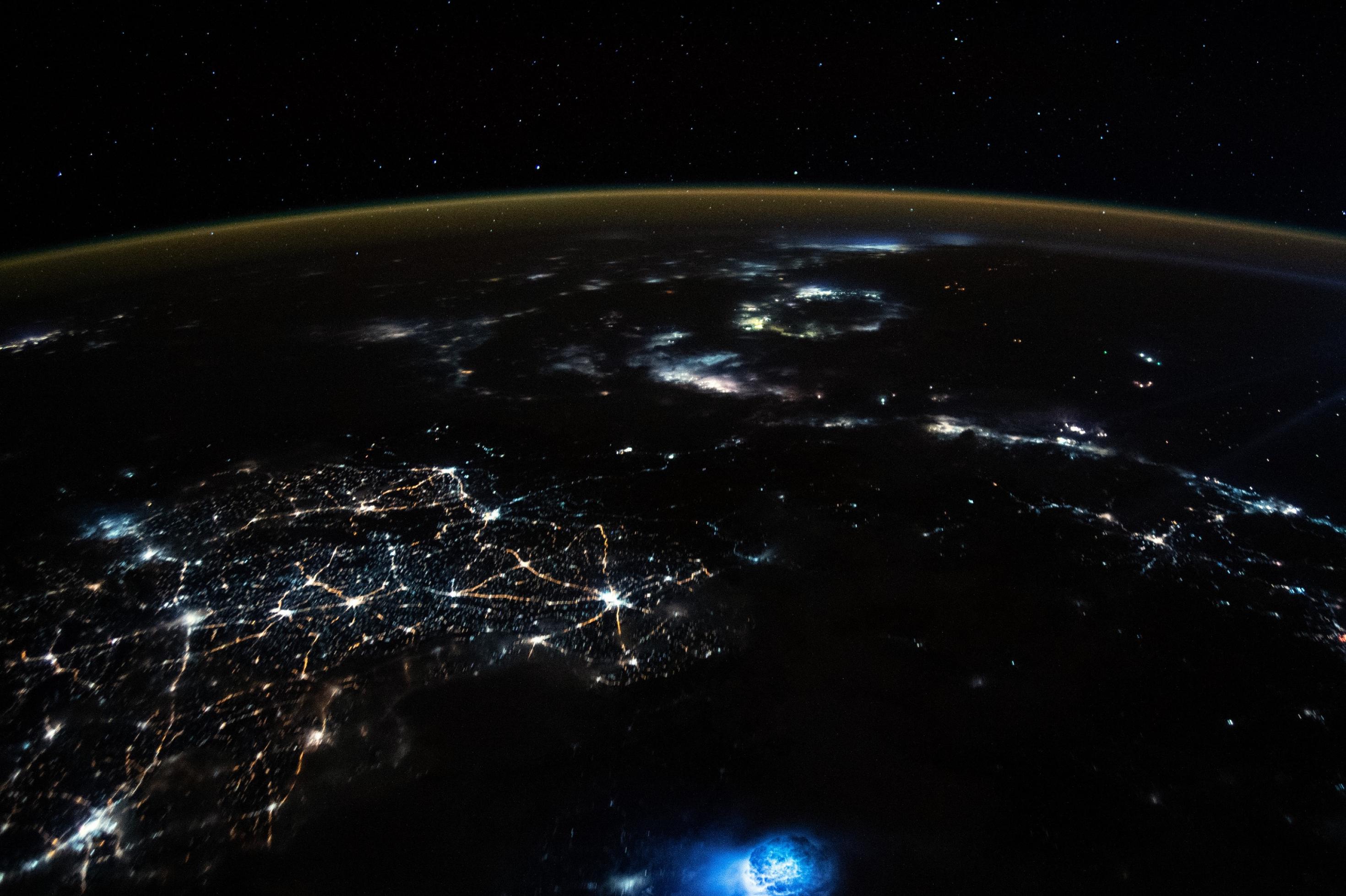 Blick aus der Internationalen Raumstation auf den nachtschwarzen Planeten mit vielen Lichtern aus Städten und von Fischereiaktivität.