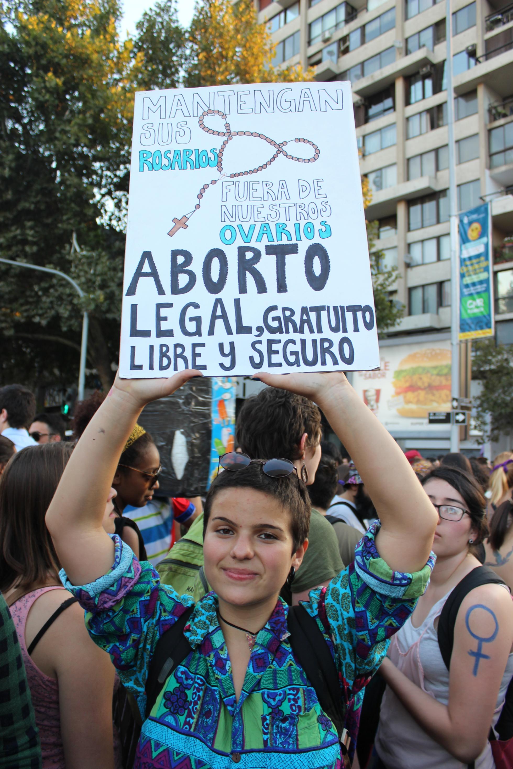 Eine Frau hält ein Schild in die Höhe mit der Aufschrift: Lasst eure Rosenkränze weg von unseren Eierstöcken – legale, kostenlose, freie und sicher Abtreibung