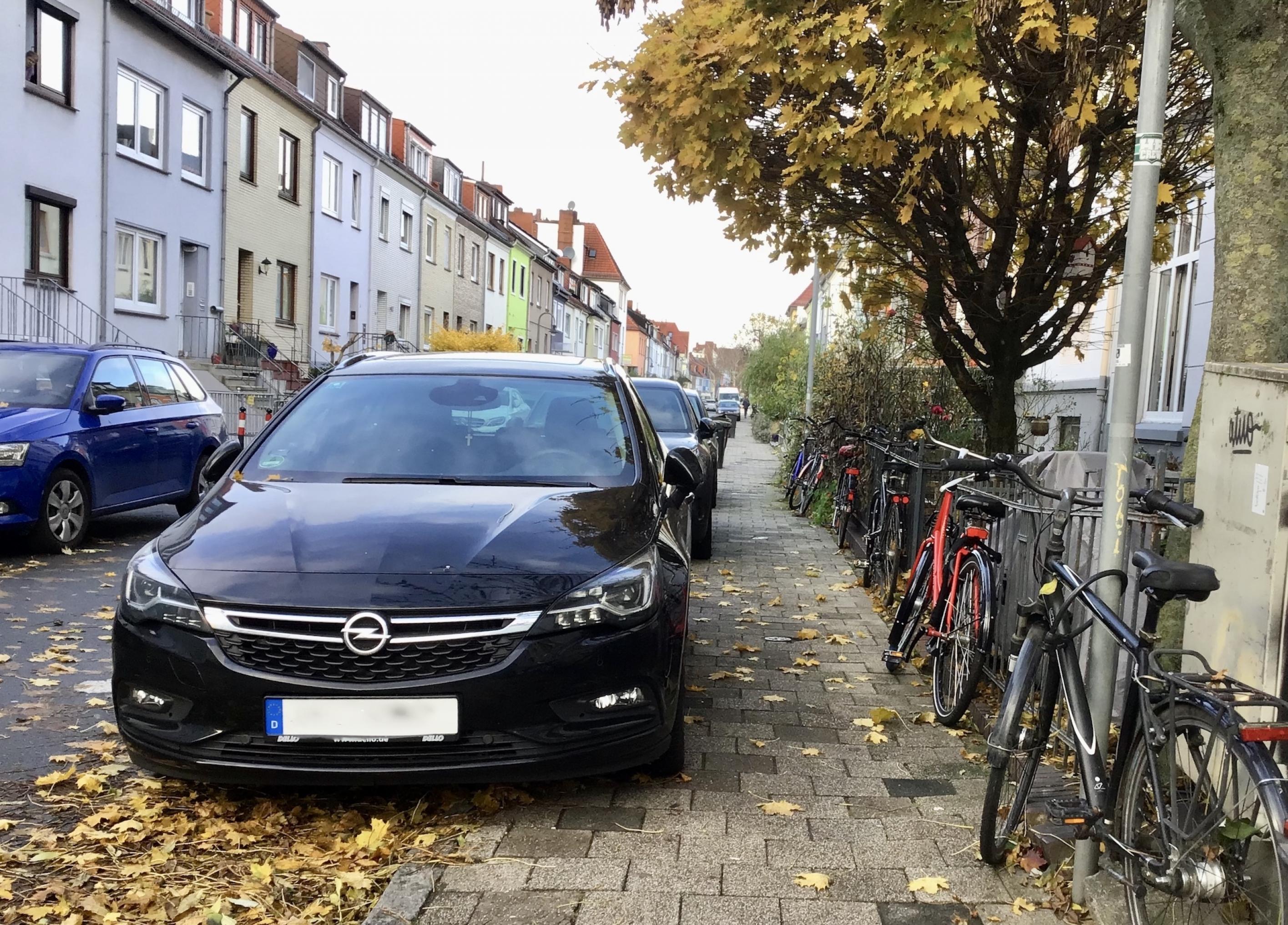 Am rechten Rand des Bürgersteigs parken Fahrräder in einer langen Reihen. Am linken Rand des Bürgersteigs parken Autos Stoßstange an Stoßstange