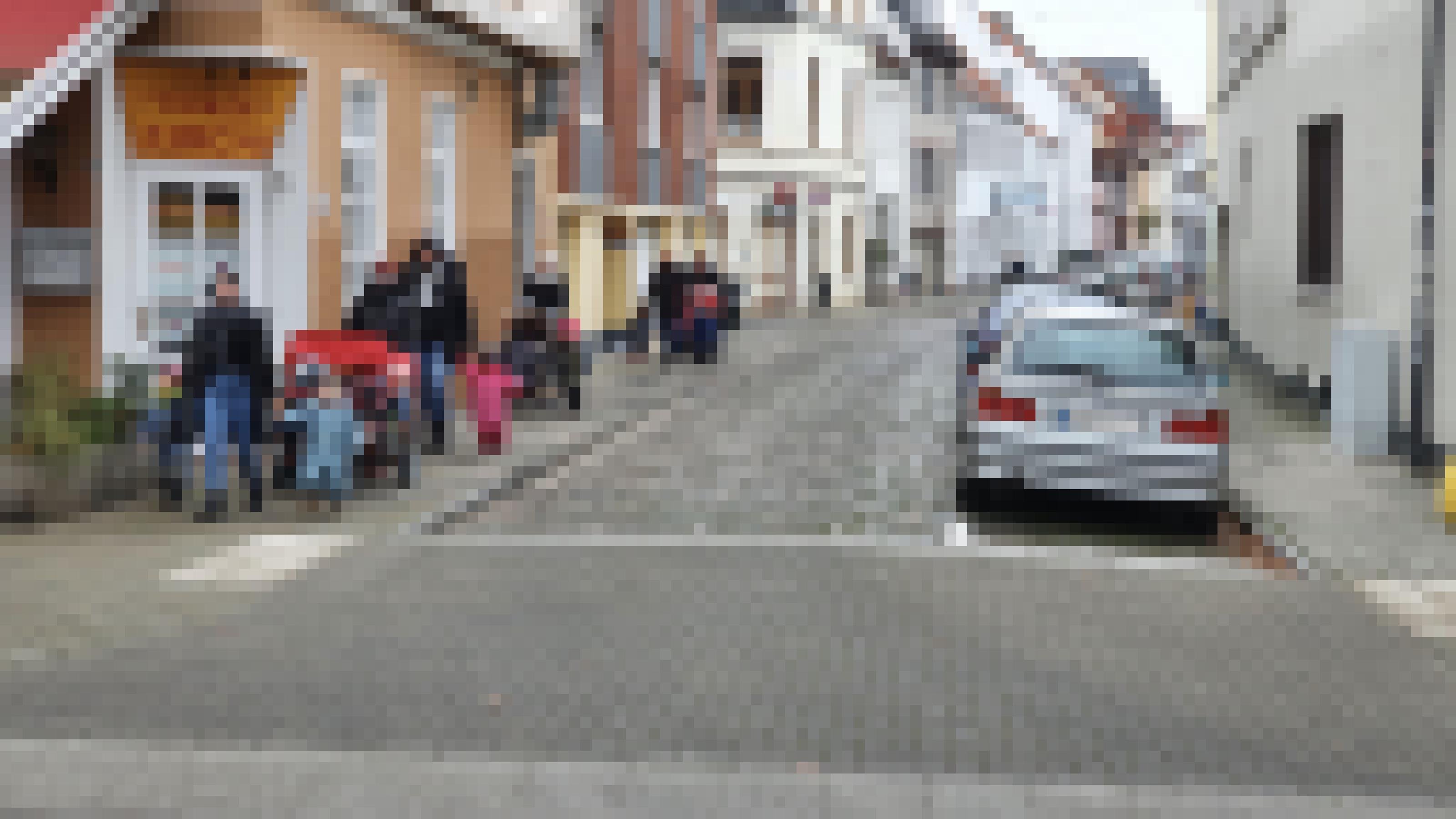 Auf dem linken Gehweg spaziert eine Gruppe Erzieher:innen mit Kindern. Am rechten Fahrbahnrand parken Autos