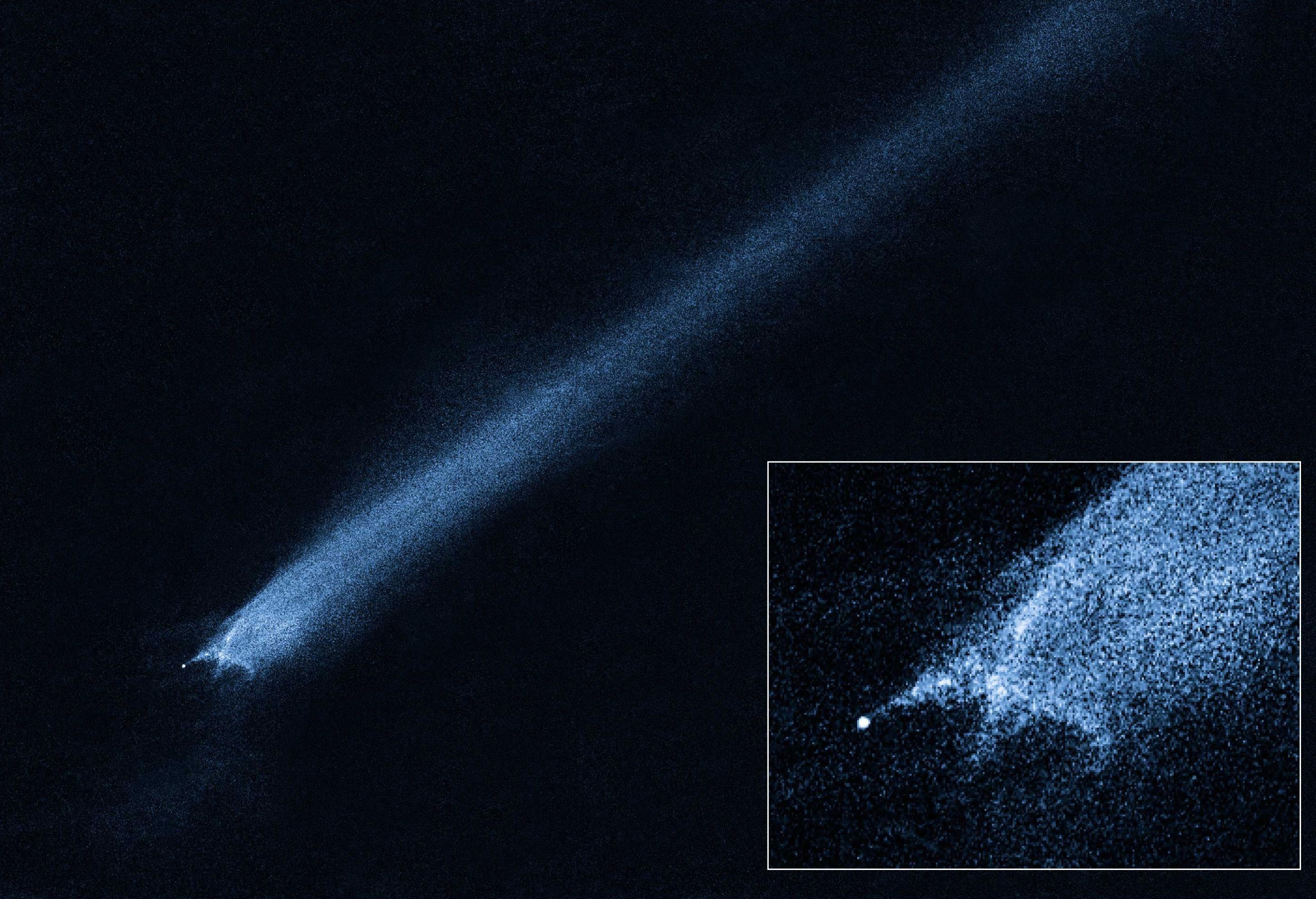 Von einem winzigen hellen Punkt geht eine grob x-förmige, blaue Wolke aus, die sich als Striemen übers gesamte Bild zieht: Ein Asteroid des Hauptgürtels mit einem Schweif.