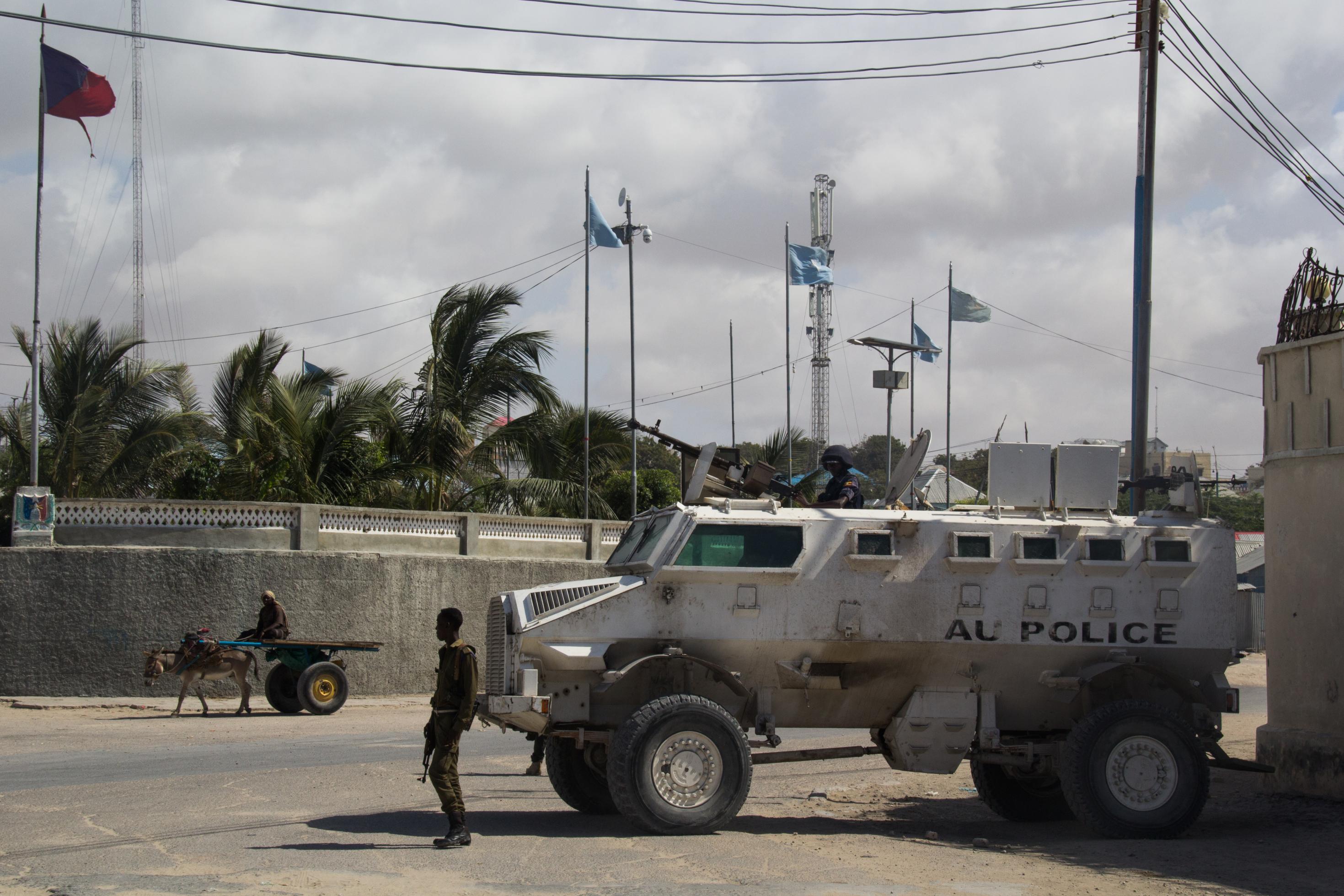 Ein weißer Panzer mit der schwarzen Aufschrift AU auf einem Platz in Mogadishu. Ein Mensch mit Eselskarren fährt vorbei, außerdem steht ein Soldat schräg vor dem Panzer.